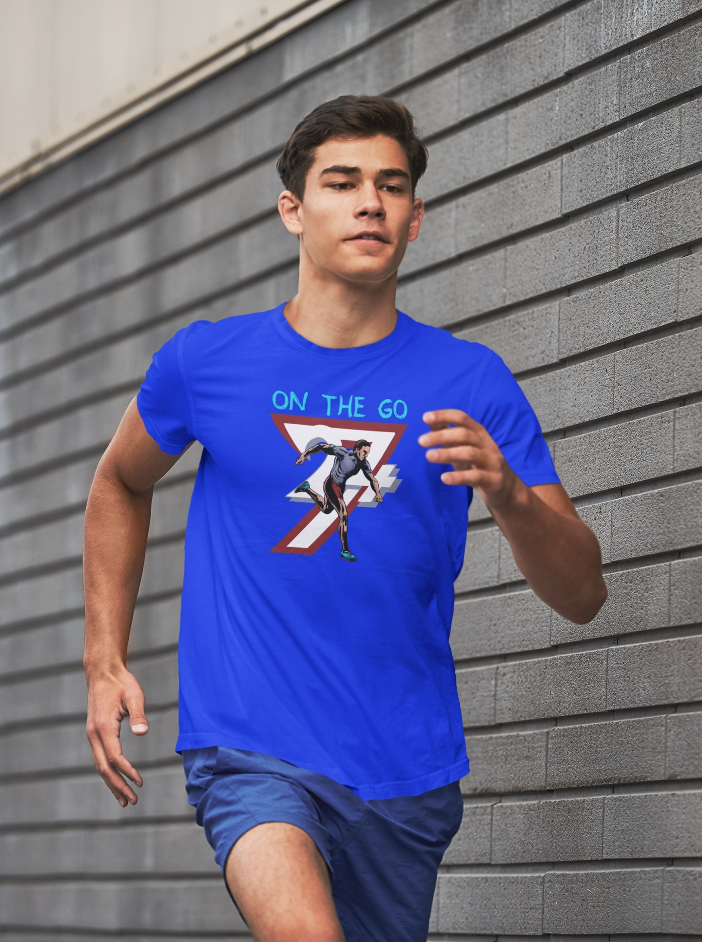 Focused male runner jogging past a modern textured brick wall in the city, wearing the royal blue hand-drawn graphic activewear tee in motion.