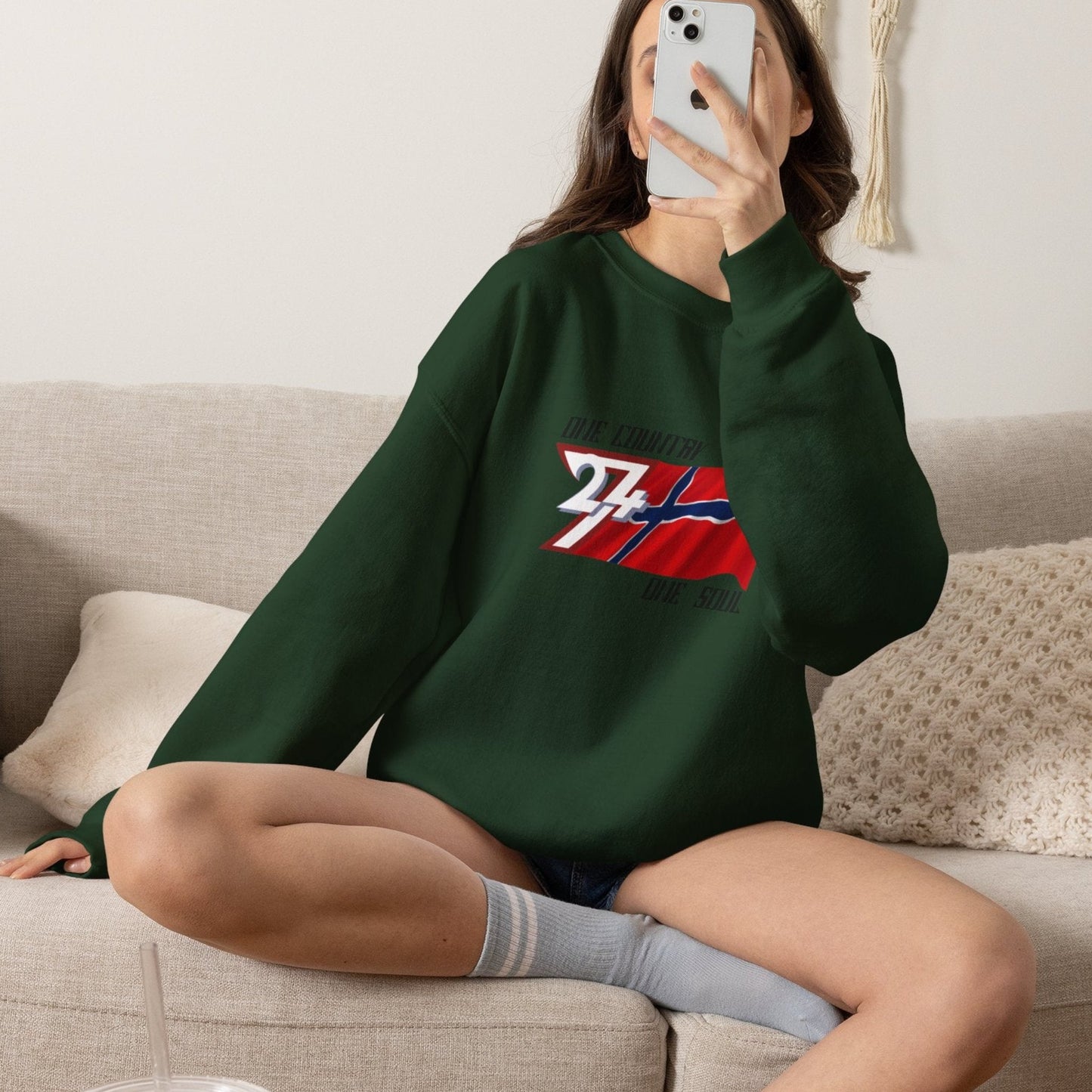 Female model wearing the deep forest green Norwegian flag pullover, taking a selfie.