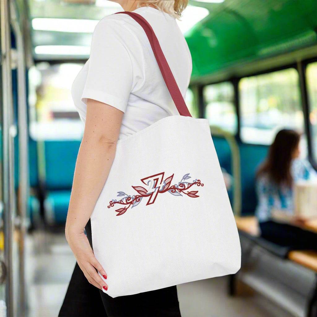 Large tote bag with red handle and unique floral illustration hanging from a shoulder of a woman travelling on a bus