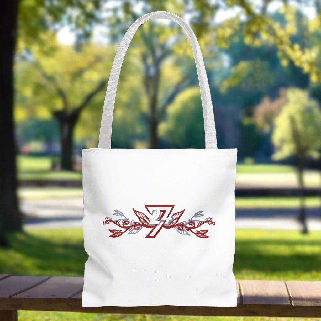 Small white tote bag with white handle and floral design placed on a bench in a park on a sunny day