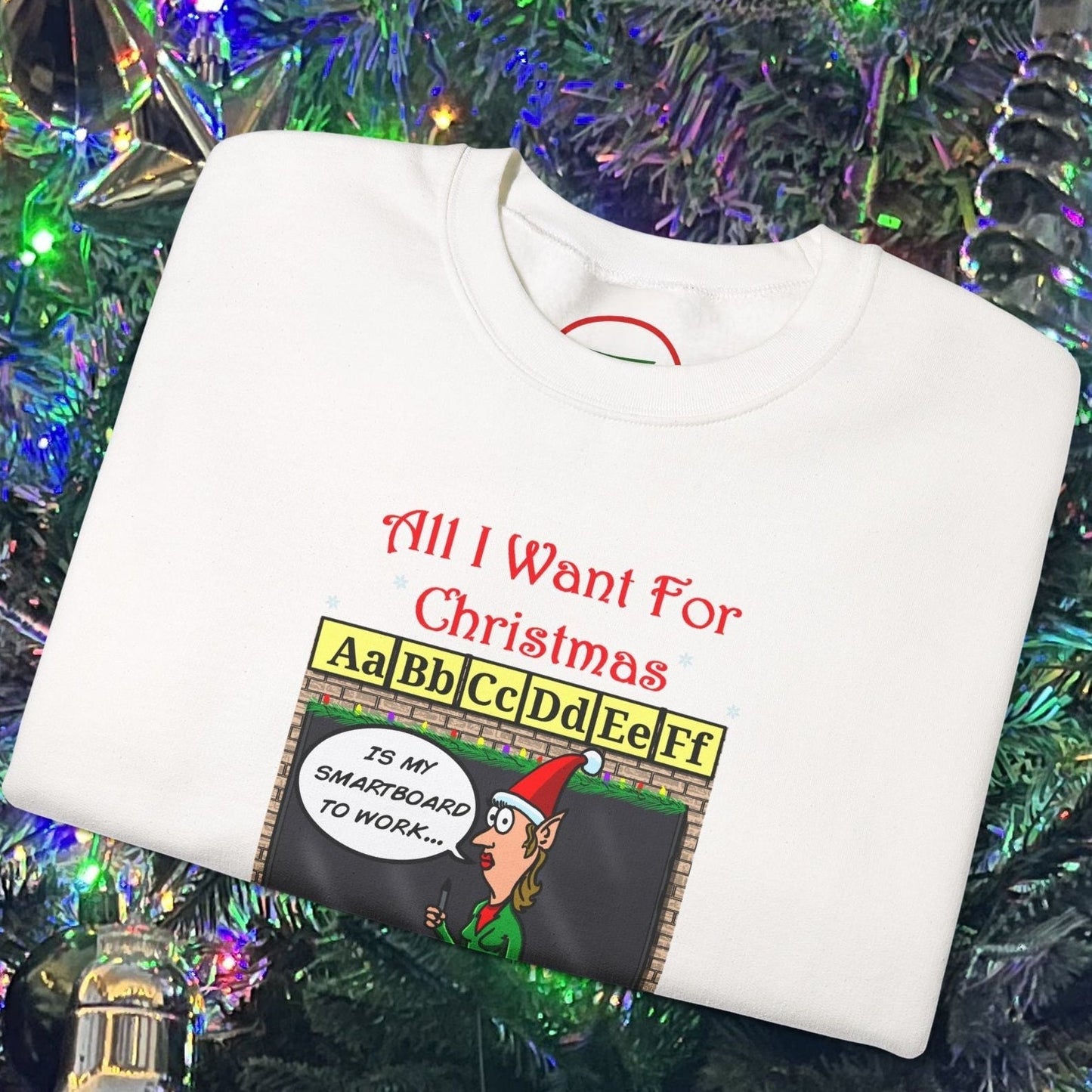 White teacher Christmas sweatshirt with funny cartoon comic design and holiday classroom theme folded on decorated Christmas tree background