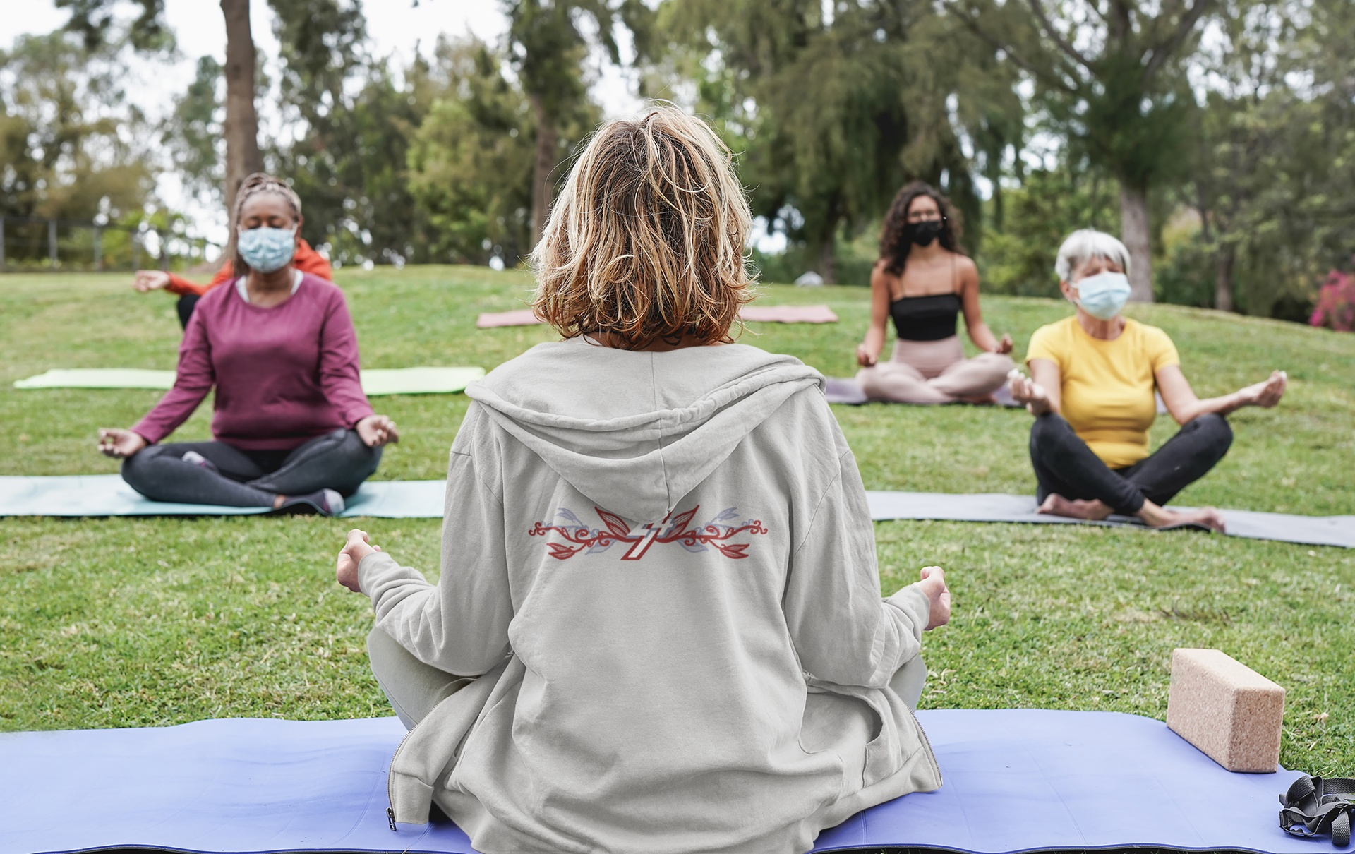 Woman sitting outdoors wearing an athletic gray zip-up hoodie, showing the large elegant botanical floral back graphic.