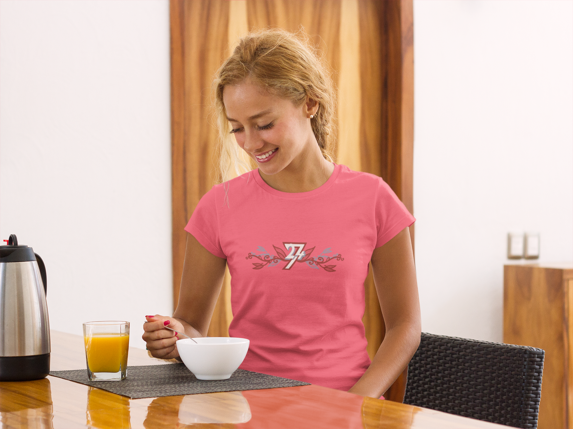 Woman wearing a semi-fitted bright pink women's tshirt featuring the elegant maroon and blue botanical 24/7 logo graphic.