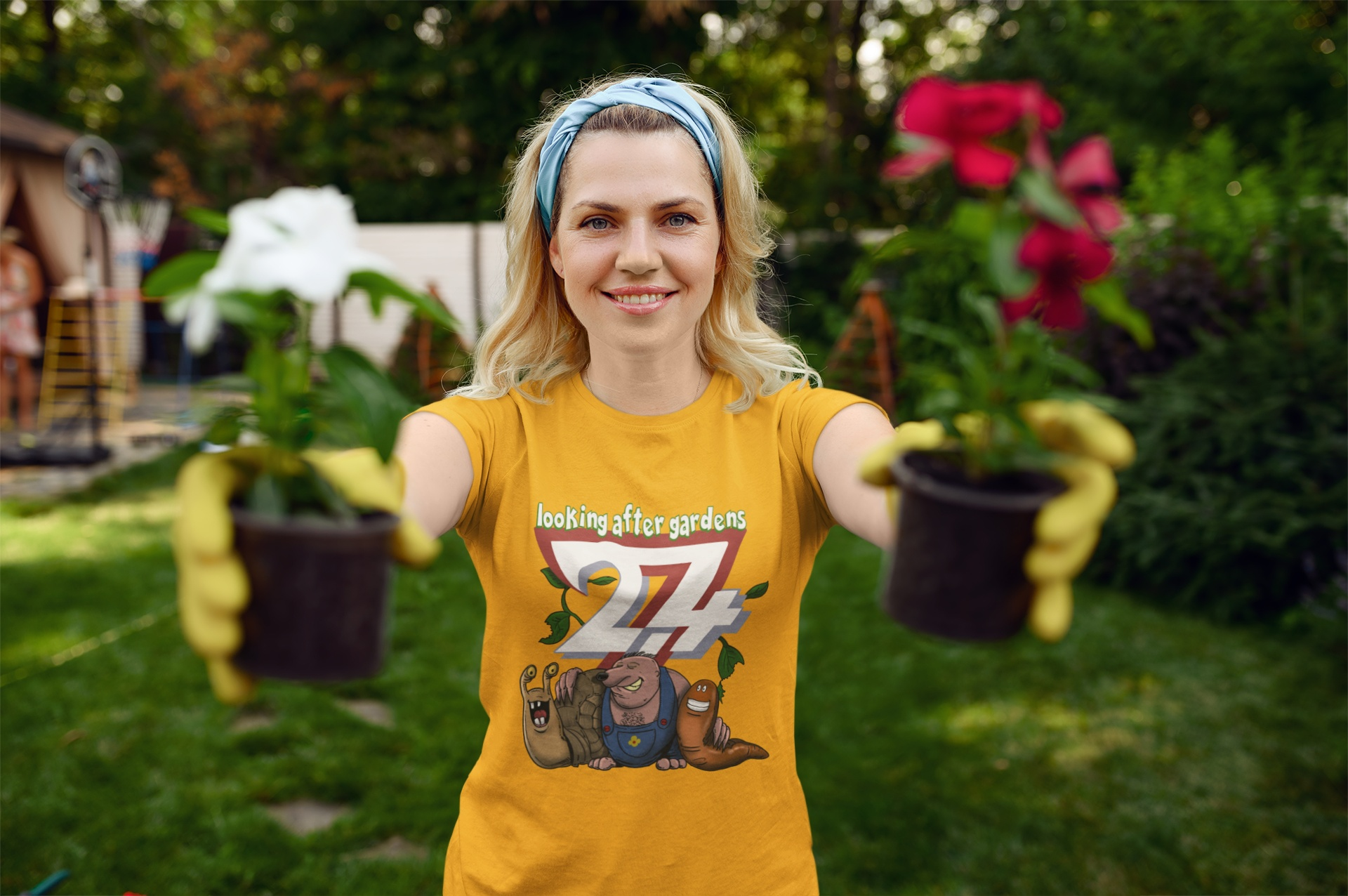 Smiling female model styling the bright yellow cute gardener gift tee, playfully holding two small potted flowers out towards the camera in a sunny yard.