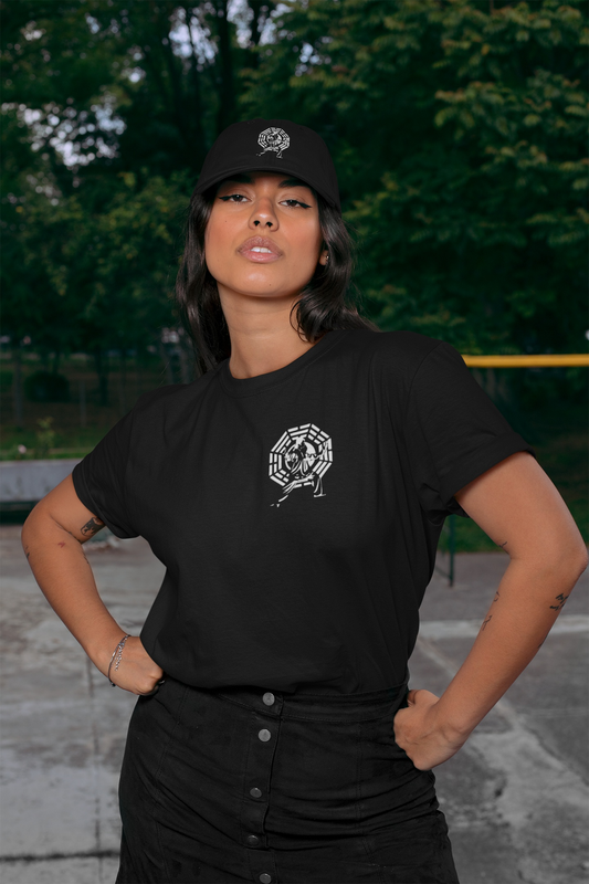 A female model posing outdoors in a park, wearing a matching black graphic tee and the black embroidered Tai Chi dad hat.