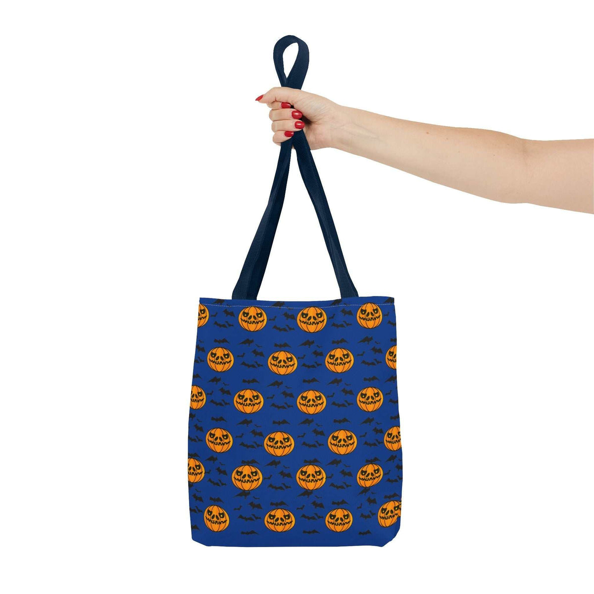 A woman's hand holding up the blue hand-drawn pumpkin pattern bag by its sturdy navy handles against a solid black background, showcasing the crisp digital print.