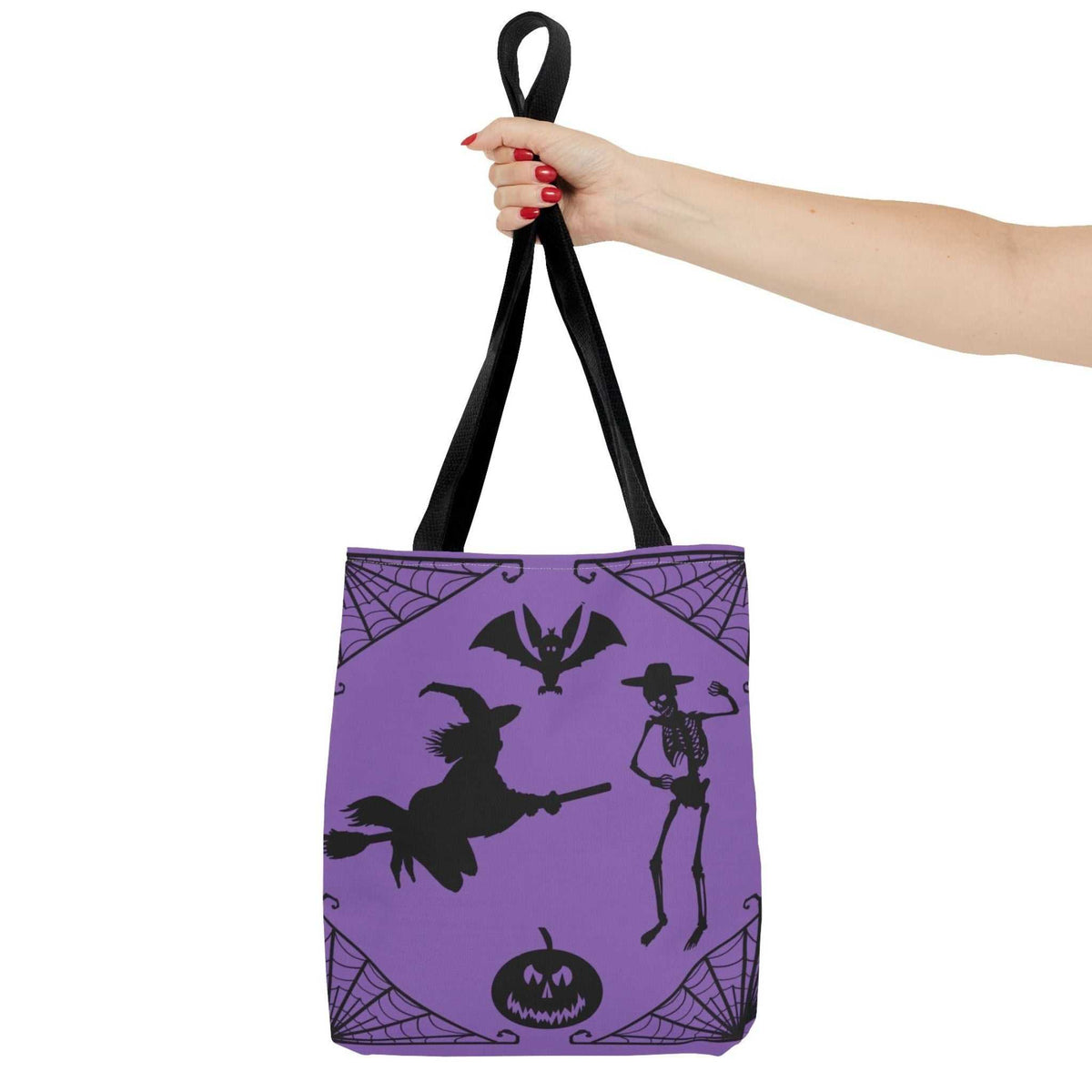 A woman's hand holding up the purple hand-drawn witch and skeleton bag by its sturdy black handles against a solid white background, showcasing the crisp digital print.