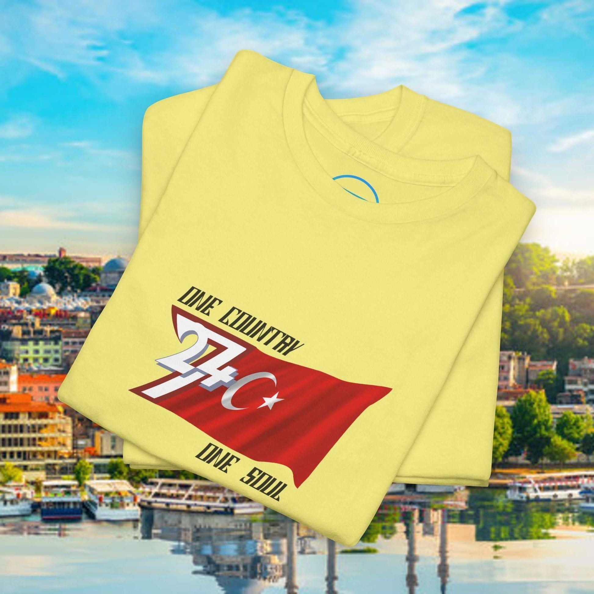 Yellow Türkiye flag graphic t-shirt with hand-drawn illustration and "One Country One Soul" text folded on cityscape background
