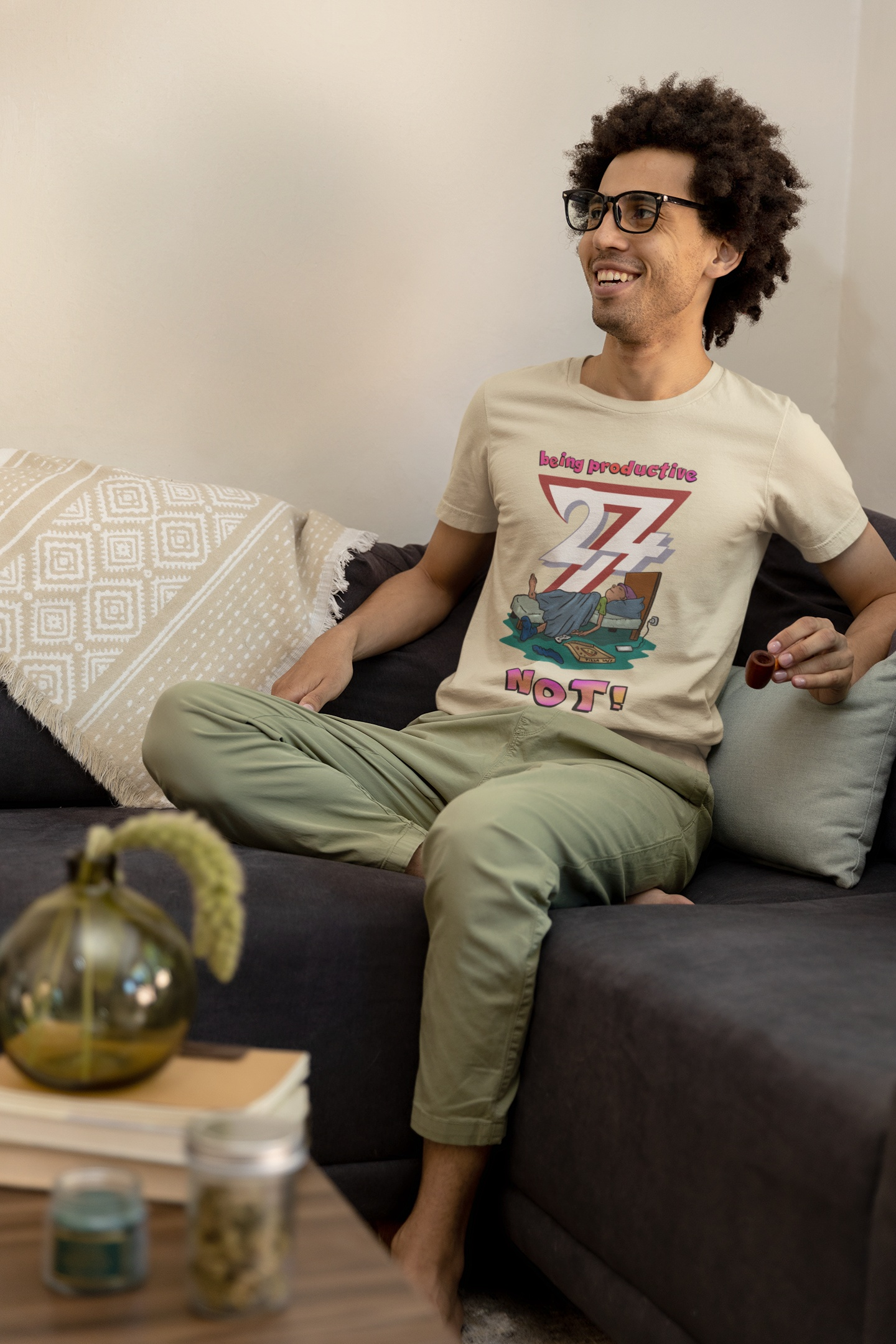 Young male model wearing the beige sarcastic student gift shirt, sitting cross-legged comfortably on a sofa with glasses and a pipe, enjoying a quiet lazy afternoon.