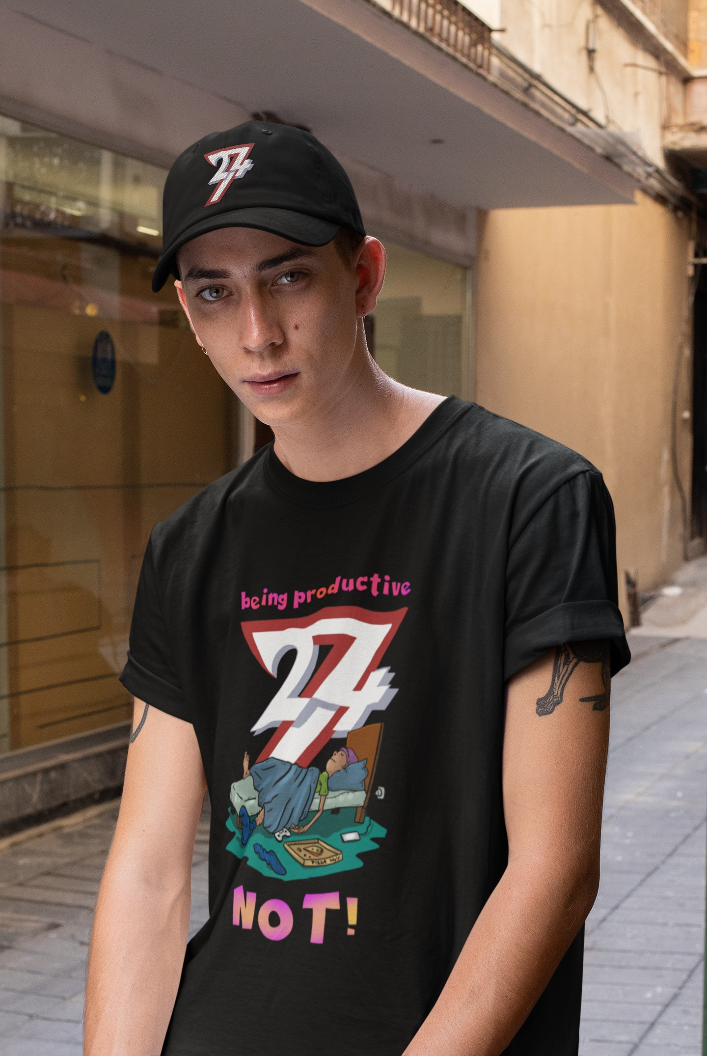 Male model showcasing the black being productive not shirt and a 24/7 dad hat, posing with a serious unmotivated expression outdoors in an urban street setting.