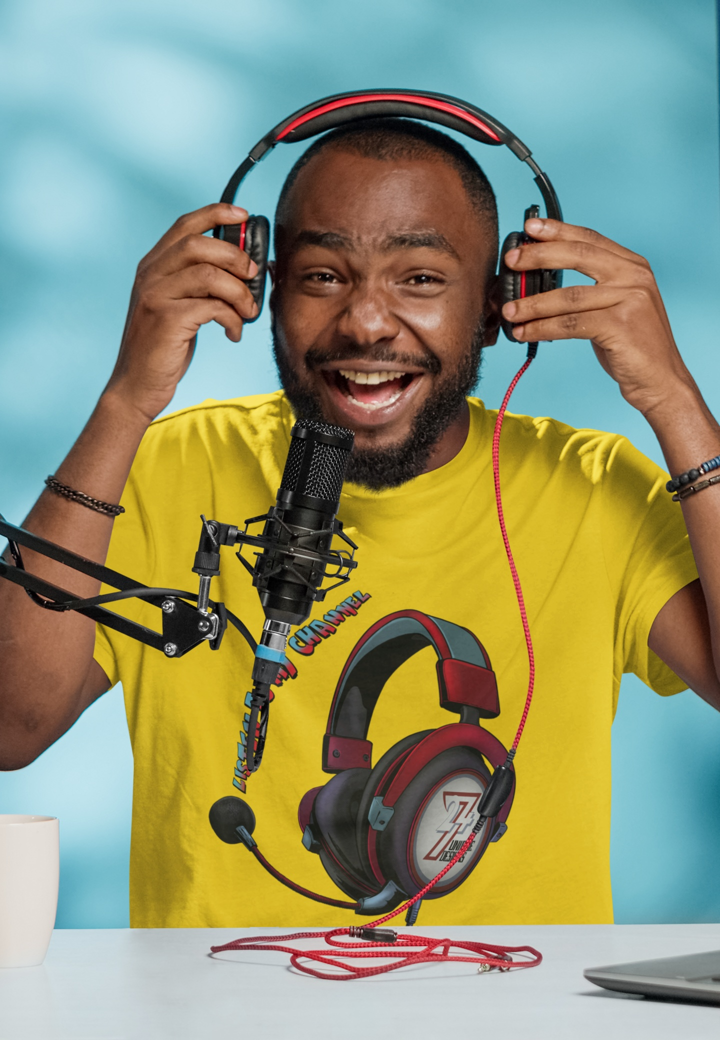 Male model wearing the bright yellow podcast host apparel featuring the red gamer headset graphic, smiling and testing audio equipment in a casual studio setting.