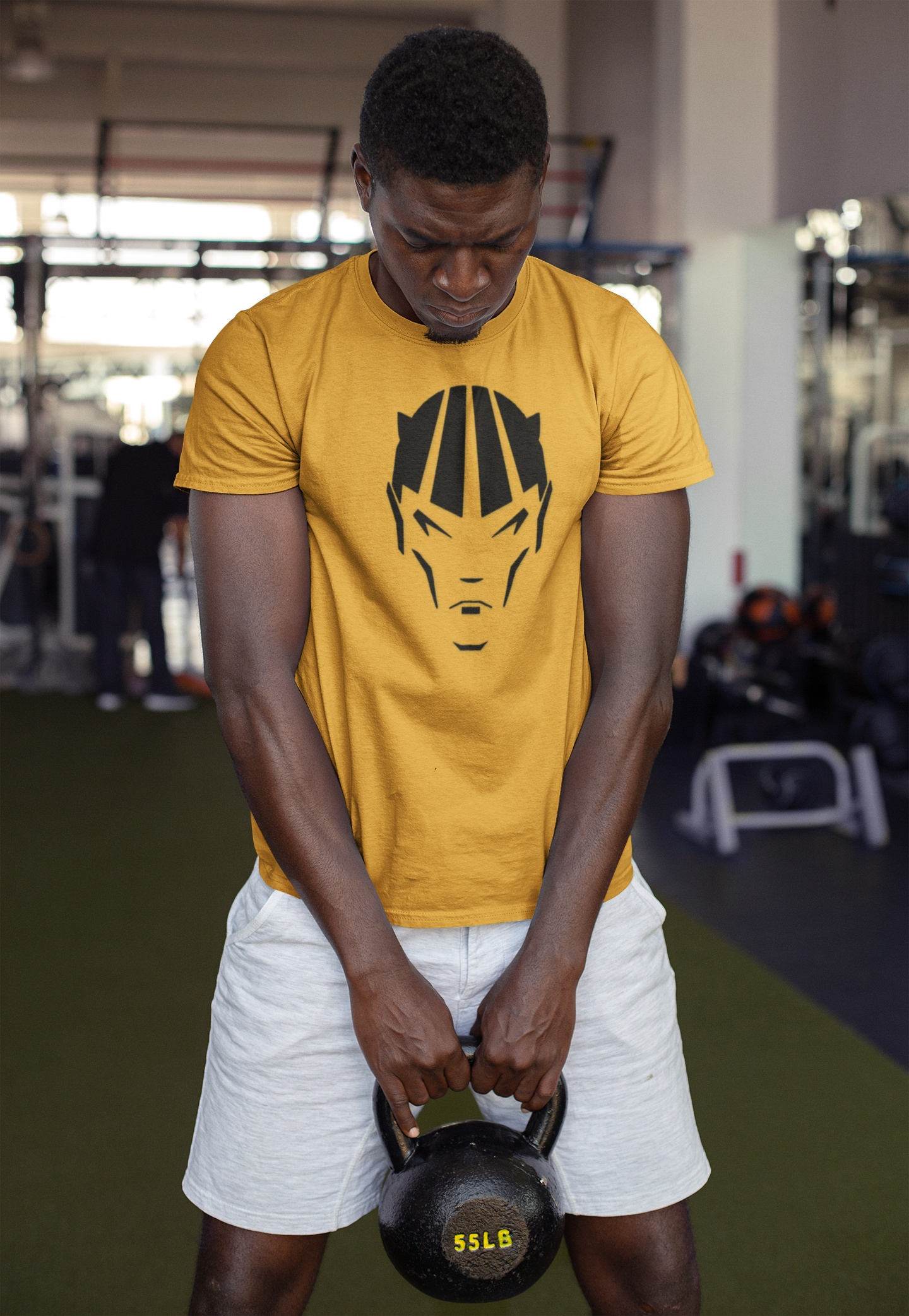 Male model wearing the gold action illustration graphic shirt while gripping a heavy kettlebell in a gym setting.