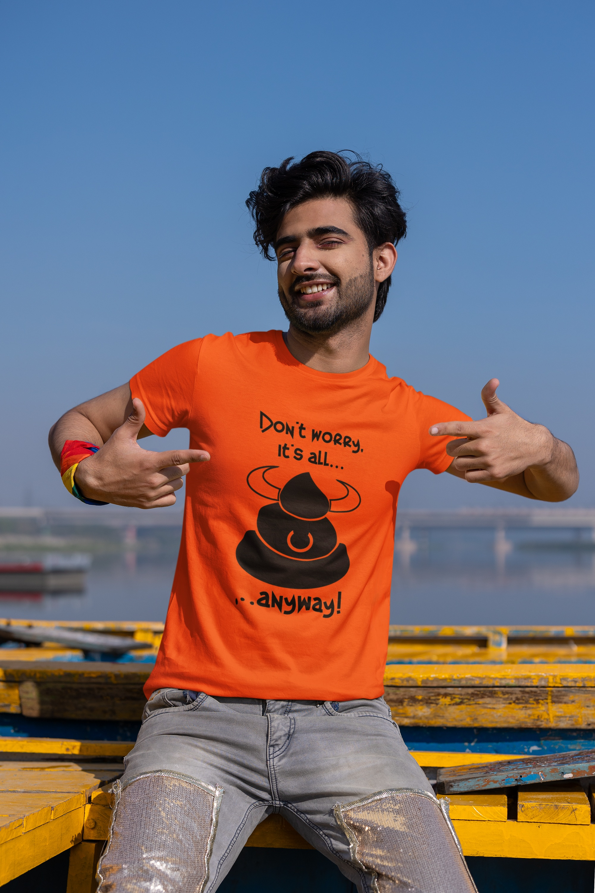Male model styling the orange funny BS t-shirt, showcasing the relaxed tubular fit sitting on wooden planks by the water
