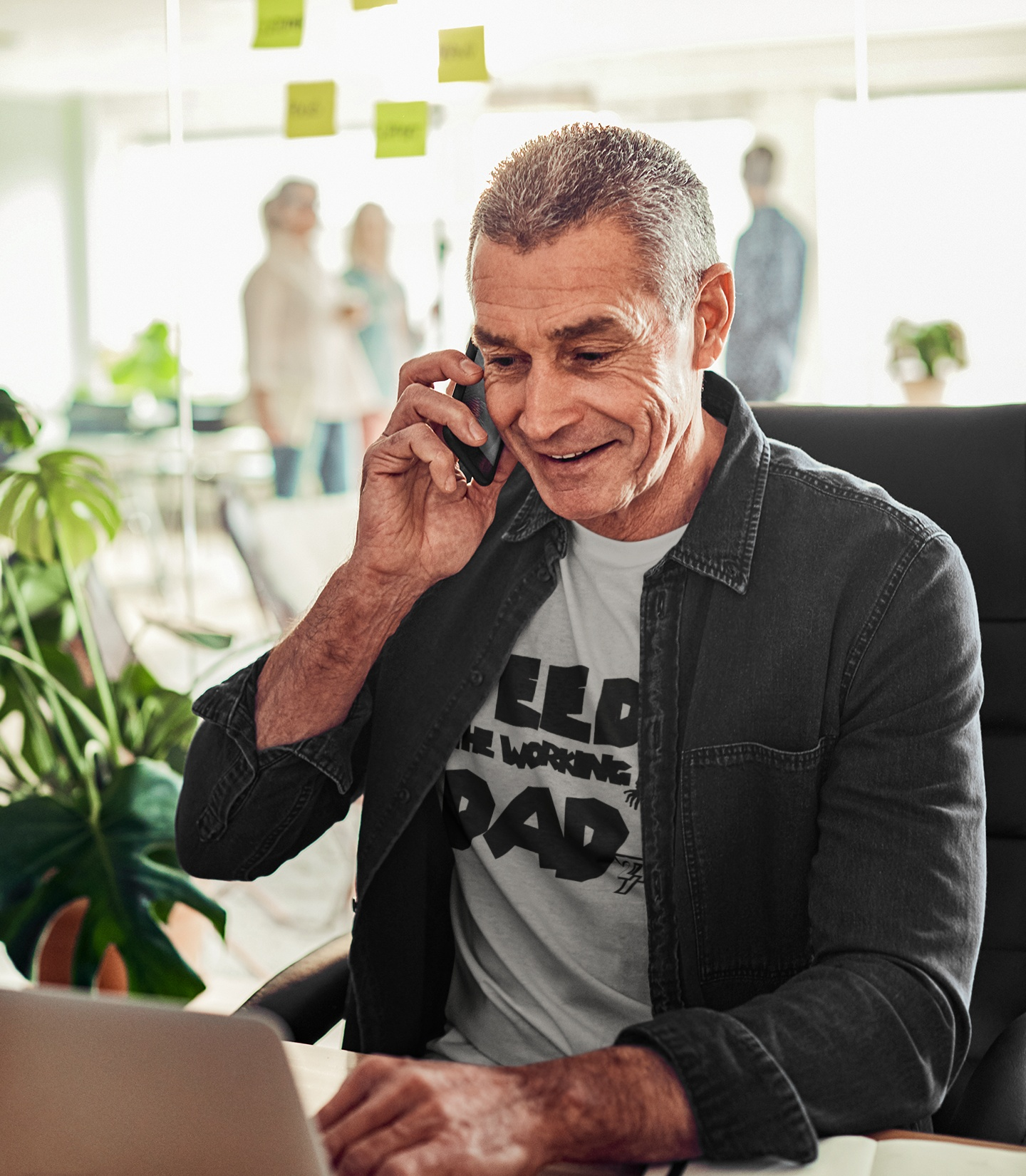 Smiling male model wearing the sport gray corporate zombie t-shirt and glasses while talking on the phone in a modern office environment, demonstrating the original comic design.