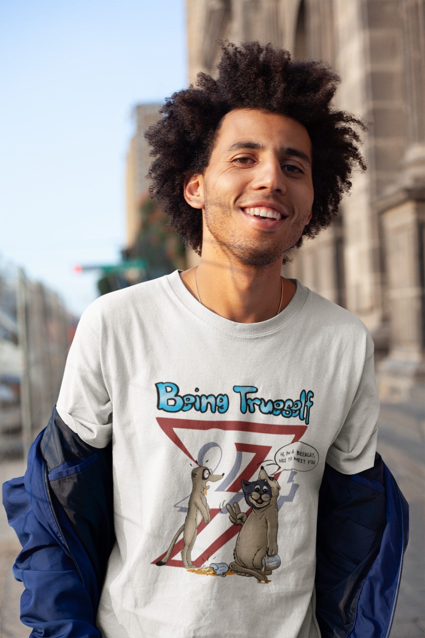 Young male model styling the white funny cat and meerkat tee under an open jacket, smiling casually on a bright urban street.