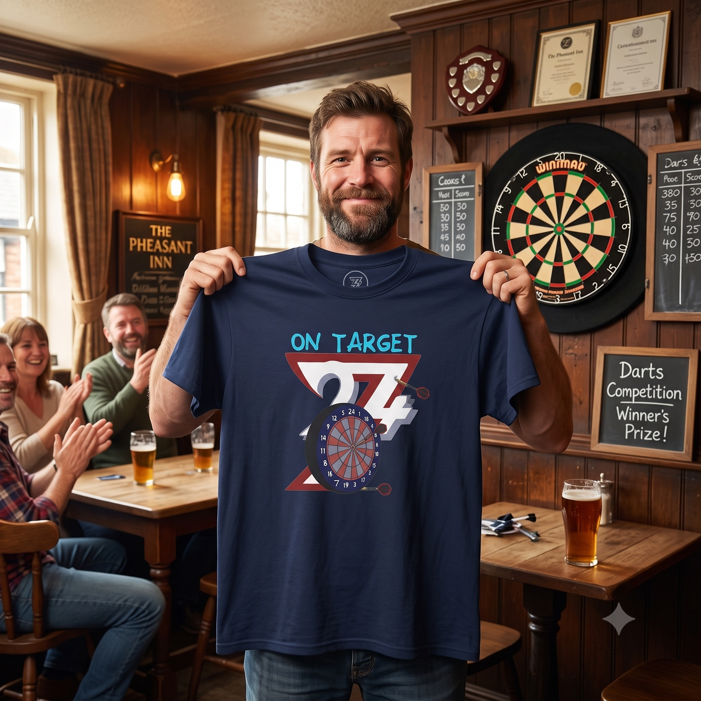 Smiling bearded man standing in a traditional pub holding up the navy blue vintage darts graphic tee, with a dartboard on the wall and friends clapping in the background.