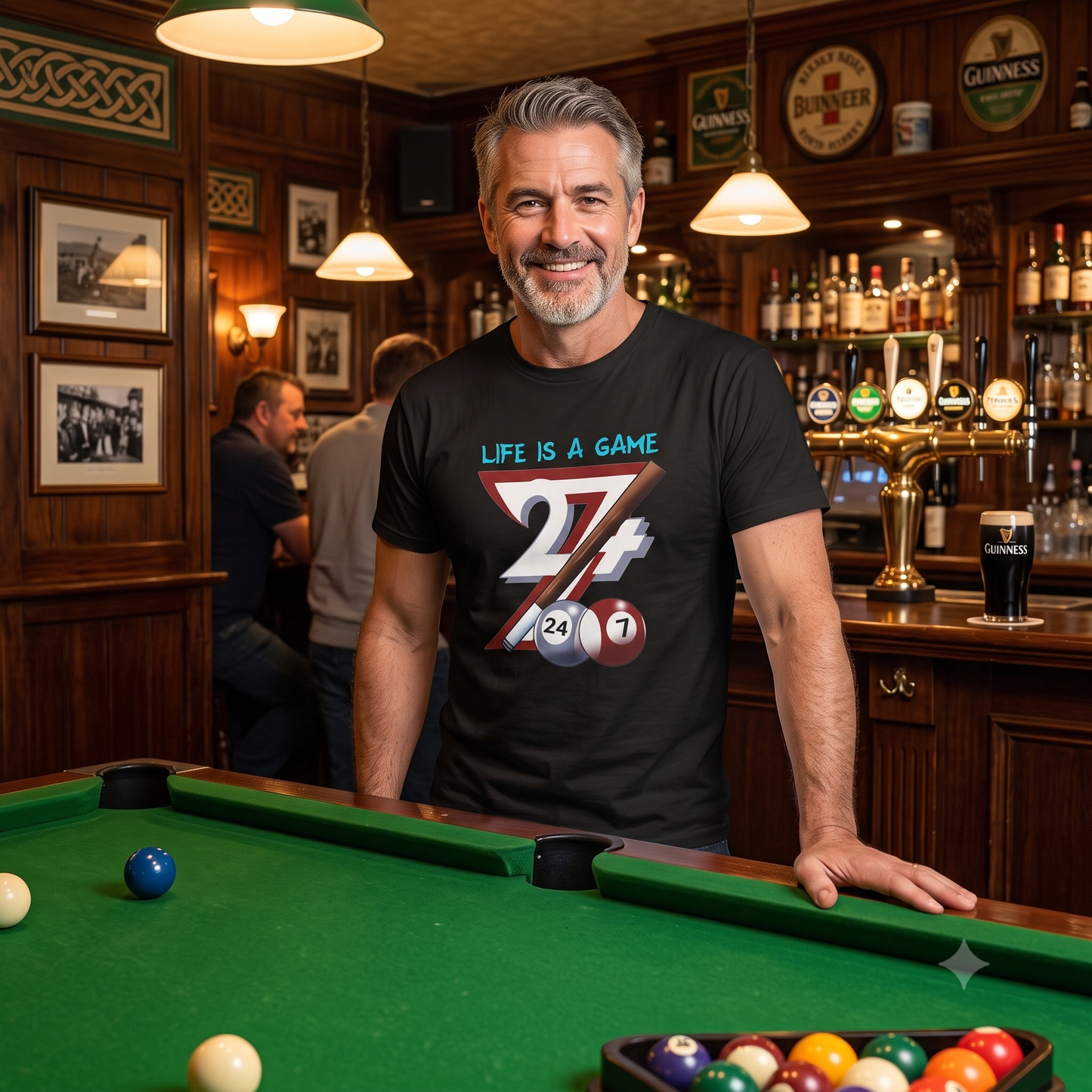 Smiling silver-haired man leaning casually on a pub pool table, wearing the black hand-drawn pool player shirt, capturing the relaxed confidence of game night.