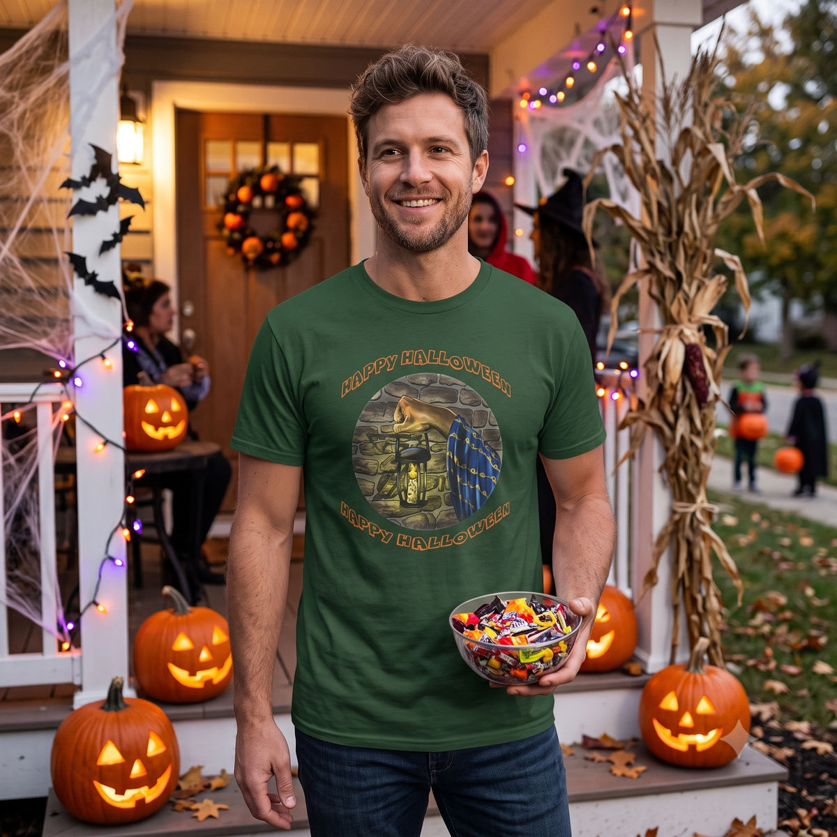 Smiling man standing on a decorated Halloween porch handing out candy, wearing the dark forest green Halloween wizard graphic tee showcasing its comfortable, relaxed fit.