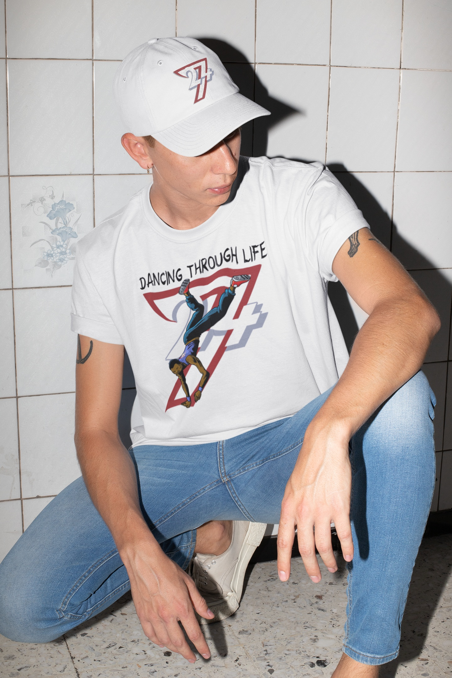 An edgy young man squatting in an urban tiled room, wearing the white hip-hop dance graphic tee and a matching white 24/7 baseball cap to showcase the ultimate street-ready aesthetic.