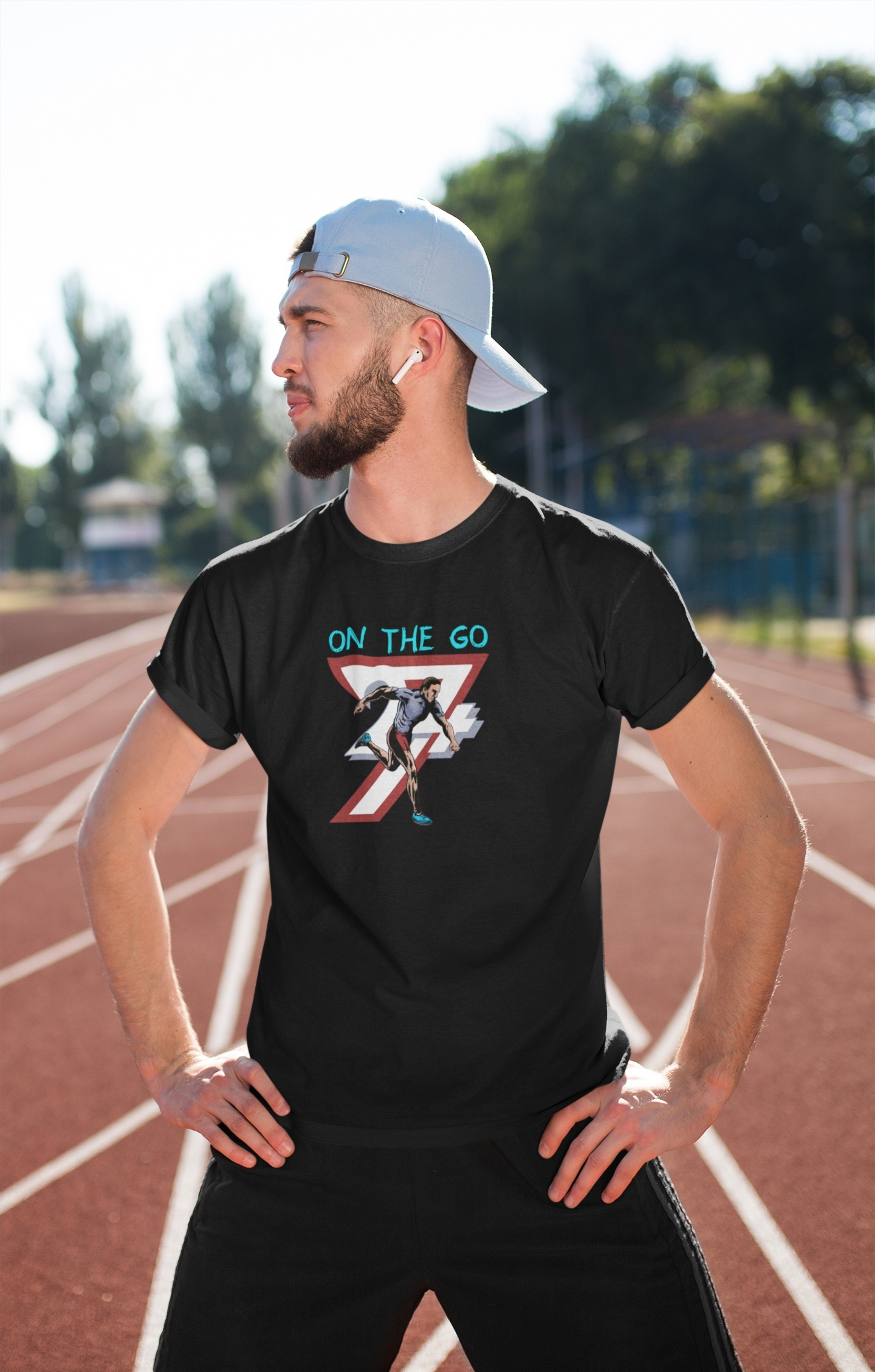 Athletic young man standing confidently on a red outdoor running track, wearing a light blue cap and the black comic style running shirt to showcase its comfortable training fit.
