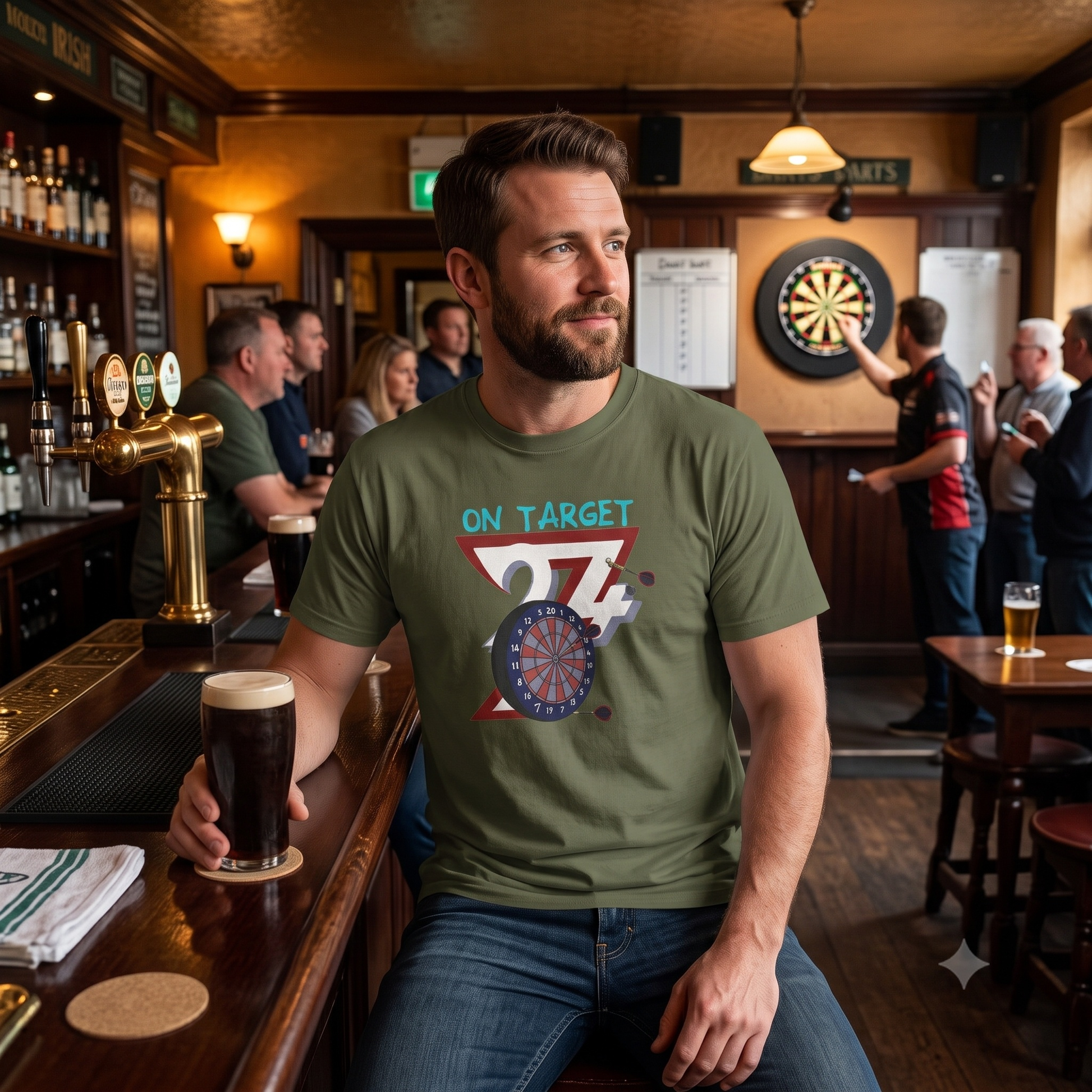 Handsome man sitting at a warmly lit pub bar with a pint of stout, wearing the army green dart league apparel tee while a game of darts is played in the background.