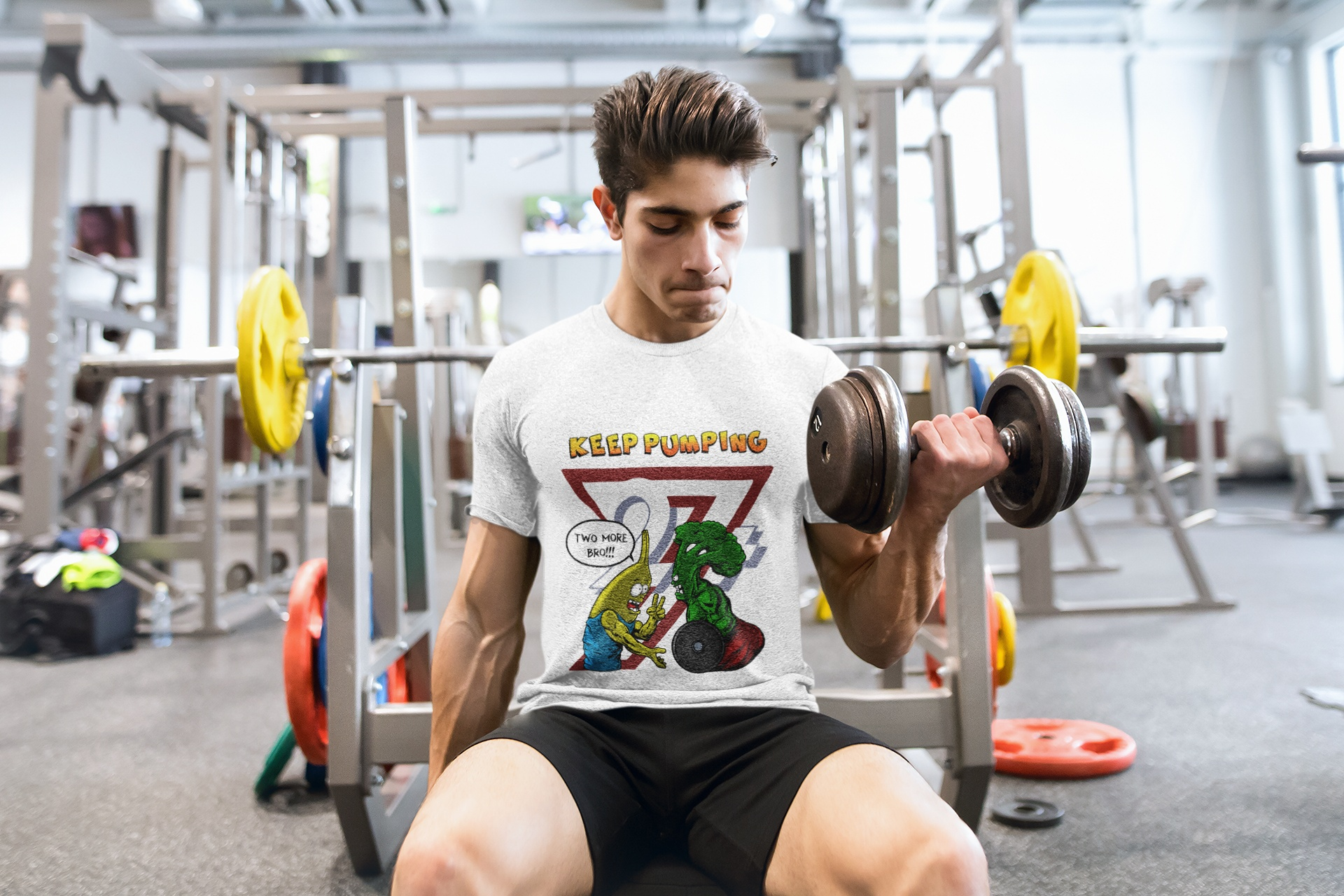 Muscular male model wearing the white funny gym buddy workout shirt, performing heavy seated bicep curls in a gym setting while showcasing the playful cartoon front graphic.