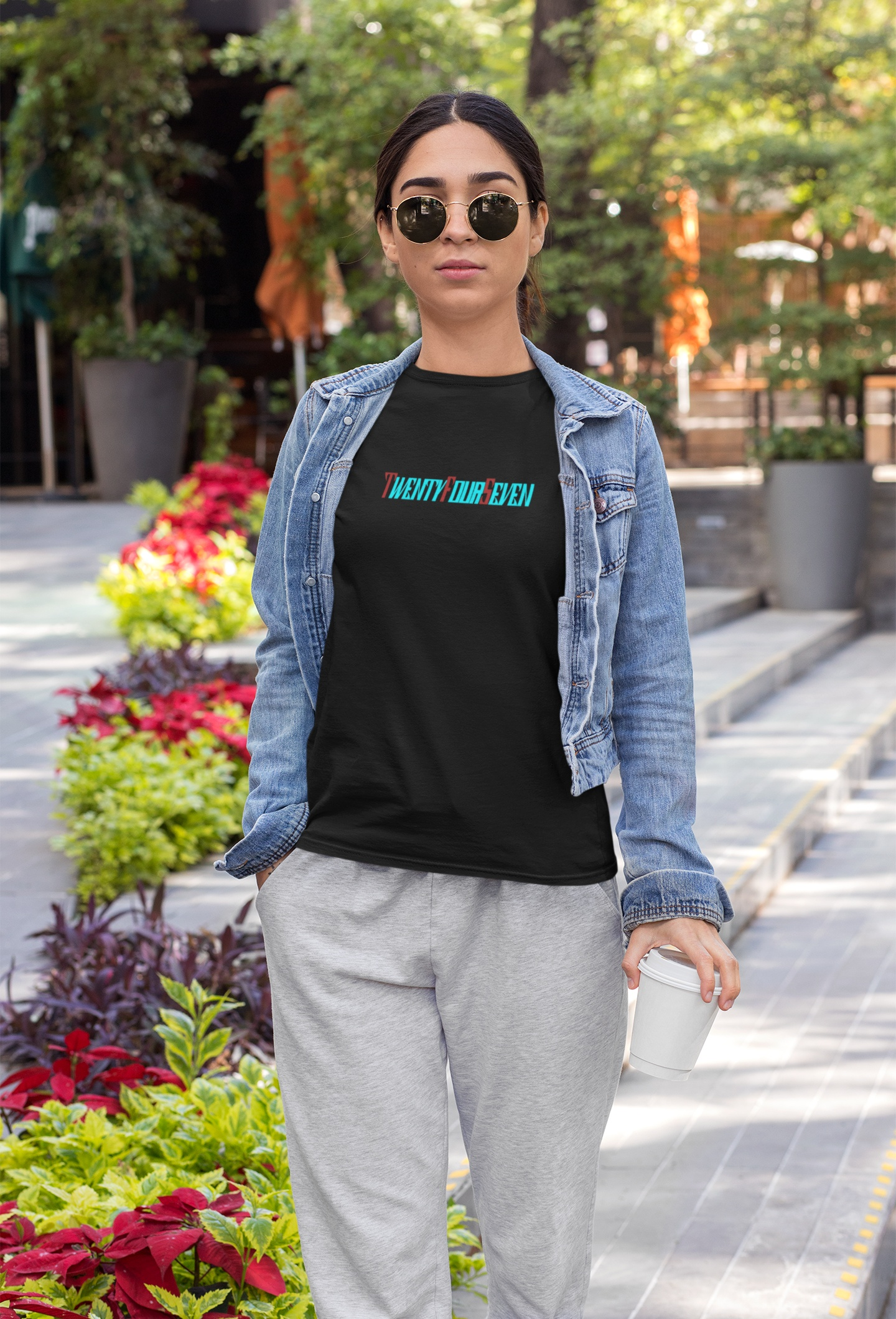 A female model confidently posing in a solid black women's t-shirt, clearly displaying the distinctive TwentyFourSeven stylized logo.