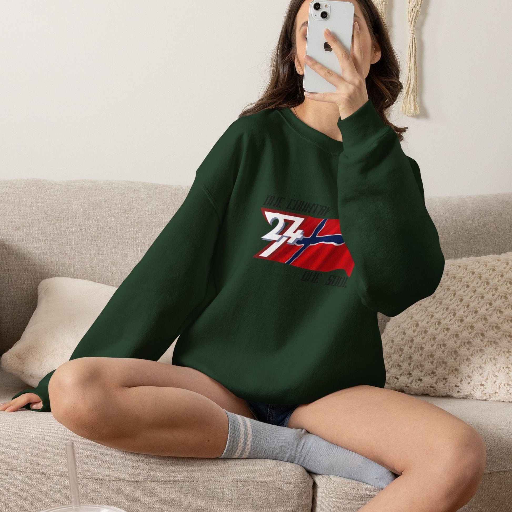 Female model wearing the deep forest green Norwegian flag pullover, taking a selfie.