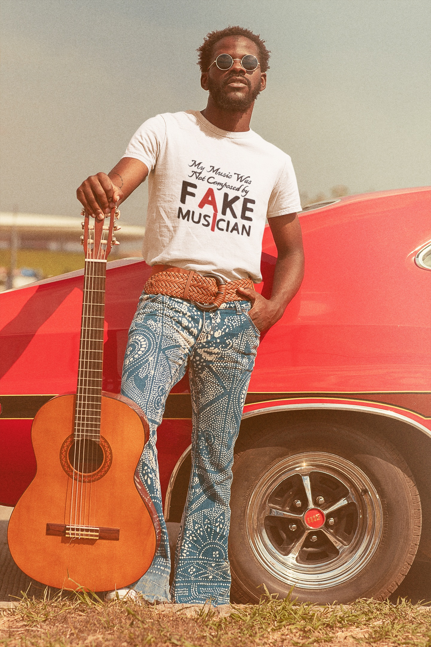 Male model wearing sunglasses and the white no AI music shirt, posing confidently with an acoustic guitar next to a classic red vintage car.