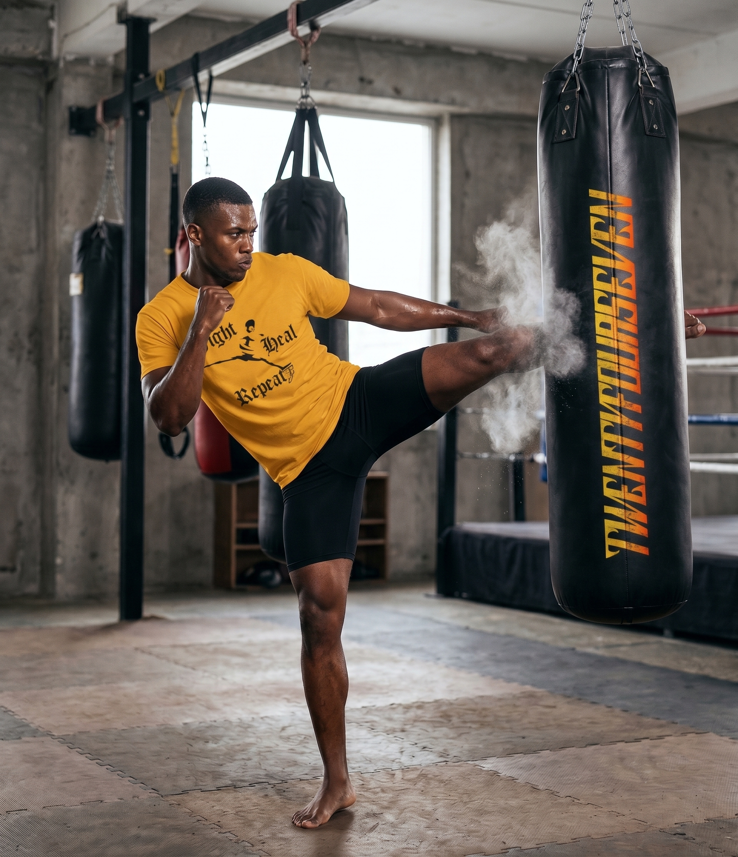 Muscular male fighter landing a powerful high kick on a black heavy bag, wearing the gold Muay Thai and kickboxing t-shirt to highlight the warrior lifestyle graphic in action.