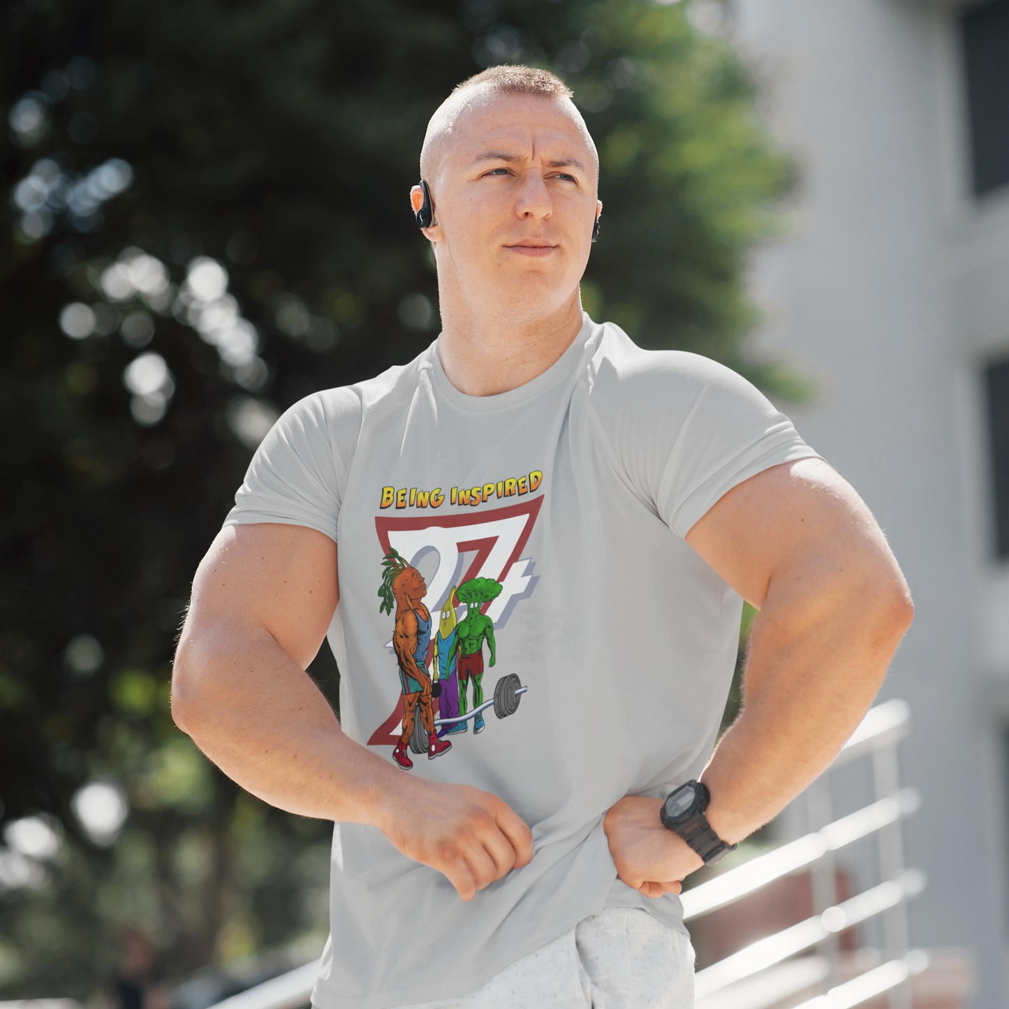 Muscular male model wearing the sport grey cartoon bodybuilding vegetables shirt, posing confidently outdoors to highlight the comfortable, athletic fit and the Being Inspired graphic.