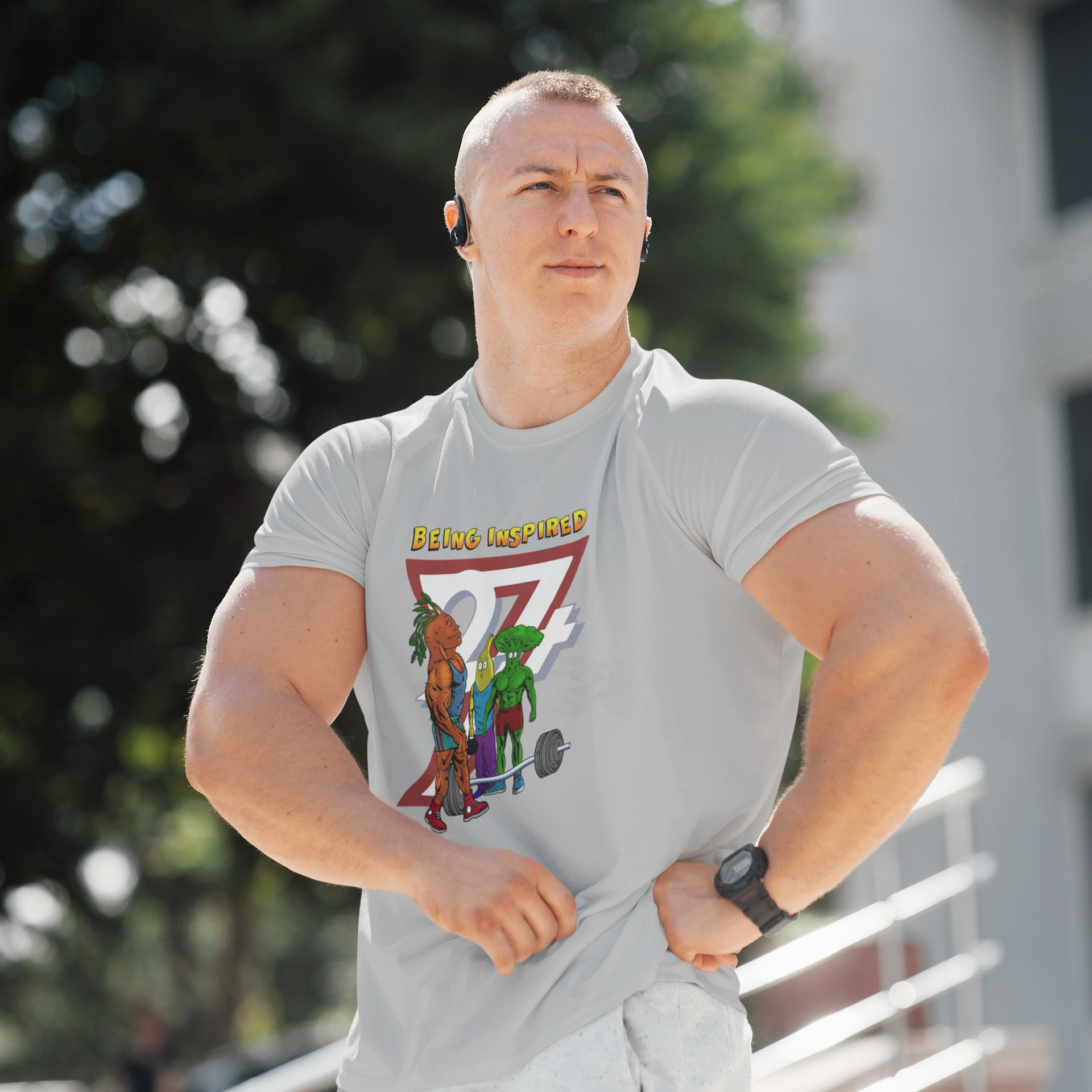 Muscular male model wearing the sport grey cartoon bodybuilding vegetables shirt, posing confidently outdoors to highlight the comfortable, athletic fit and the Being Inspired graphic.