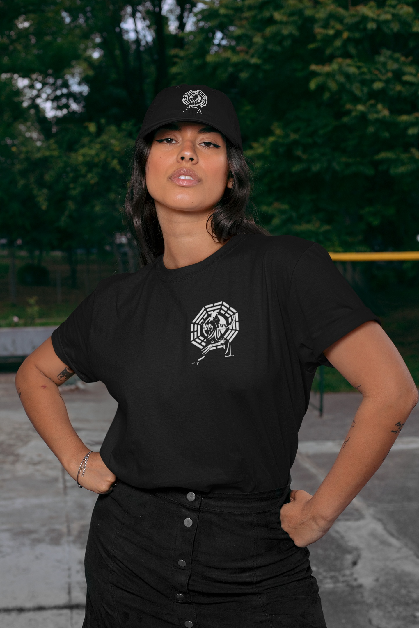 Model standing confidently in an outdoor park wearing the black minimalist Tai Chi t-shirt, perfectly styled with a matching black martial arts dad hat.