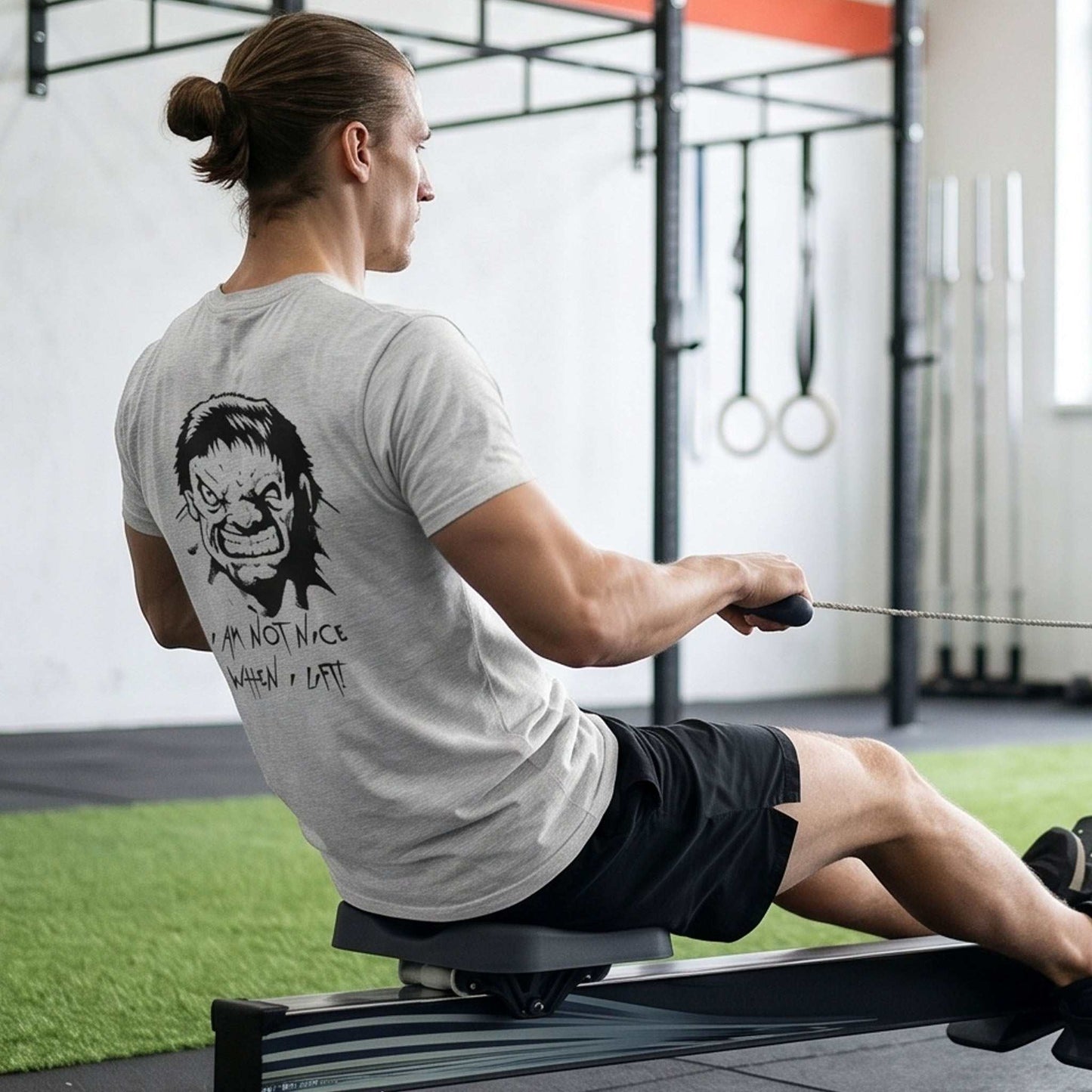 Male model wearing the ash grey gym quote graphic tee, seen from the back while performing a seated cable row in a gym to showcase the comic lifter face illustration.