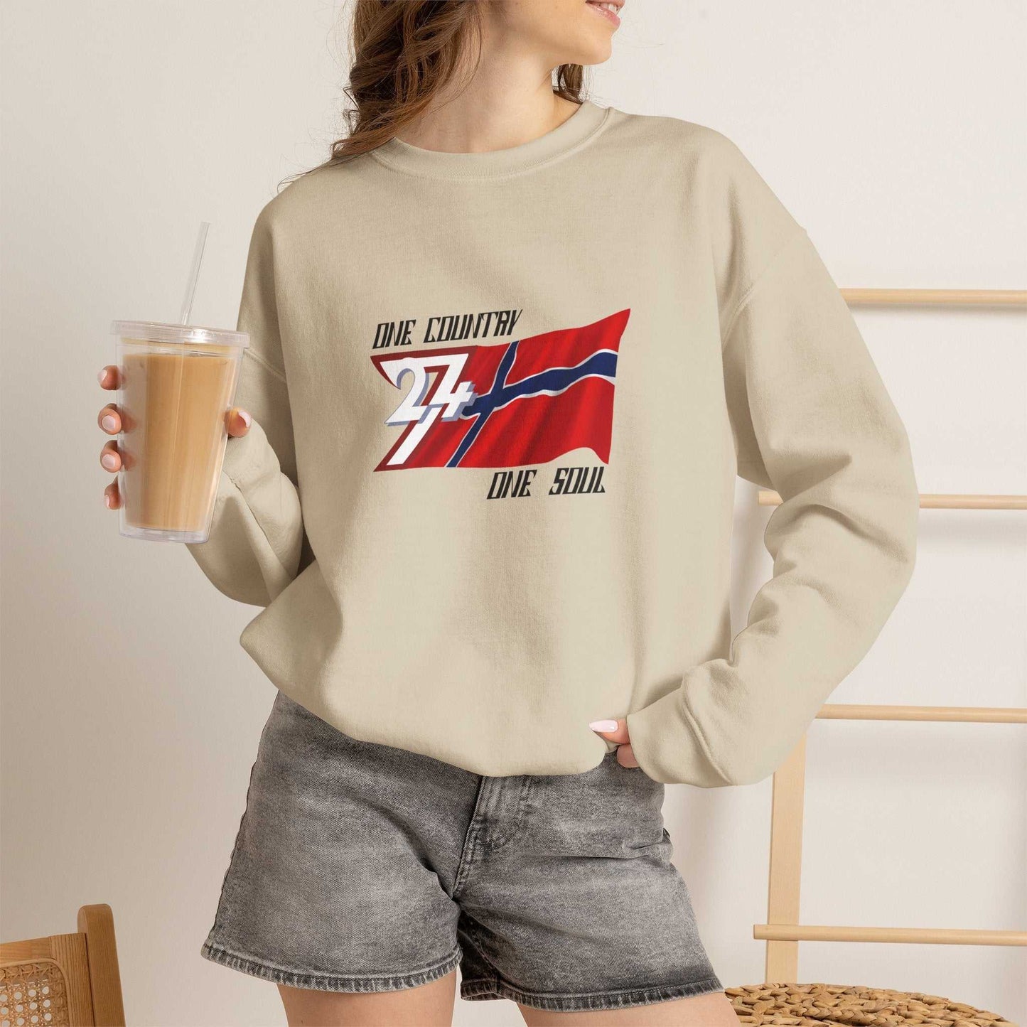 Female model styling the sand beige Norway flag crewneck sweatshirt, posing casually indoors to showcase the comfortable, relaxed fit.
