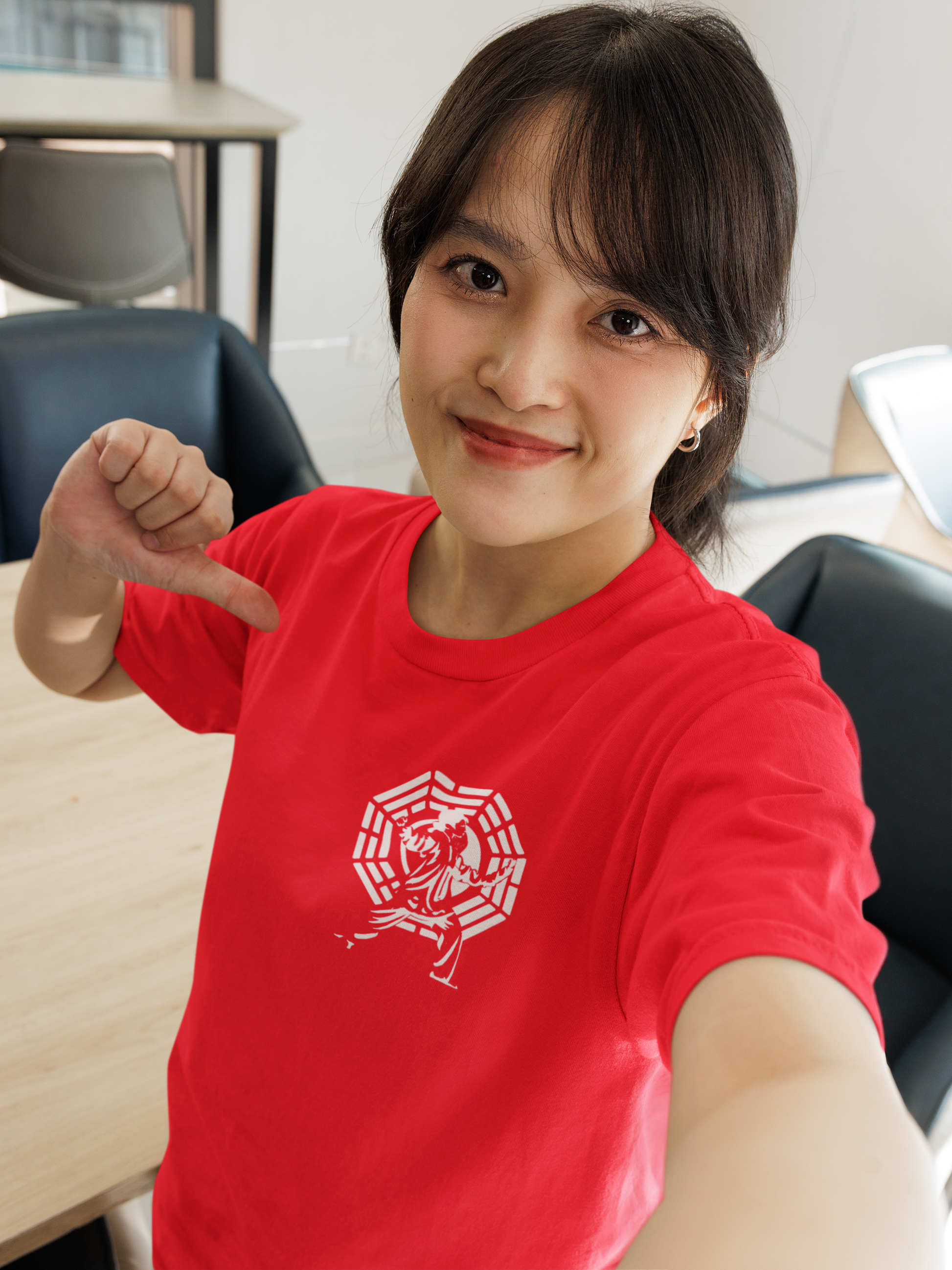 Smiling model taking a selfie and pointing confidently at the traditional Bagua chest emblem on the red minimalist Tai Chi t-shirt in a bright indoor setting.