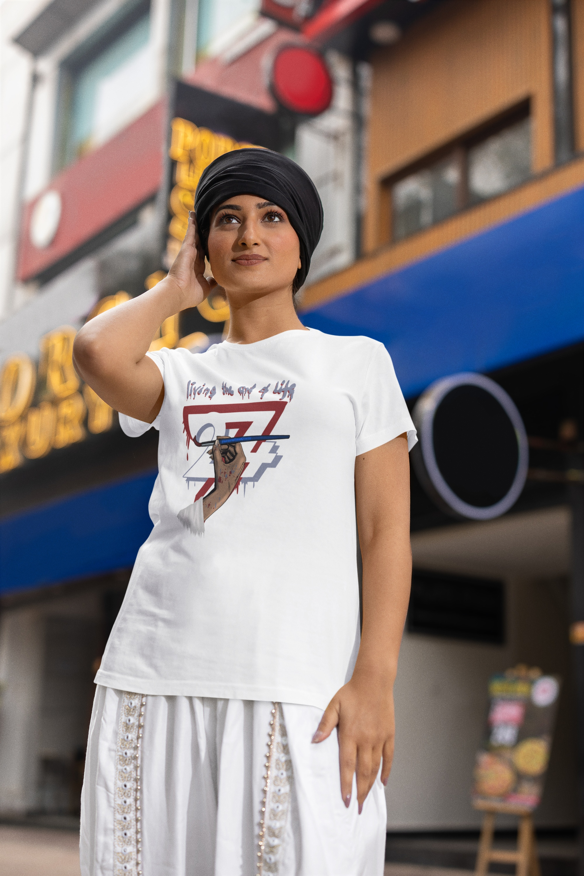 Female model wearing the white women's painter graphic tee and a black headwrap, posing outdoors on a city street.