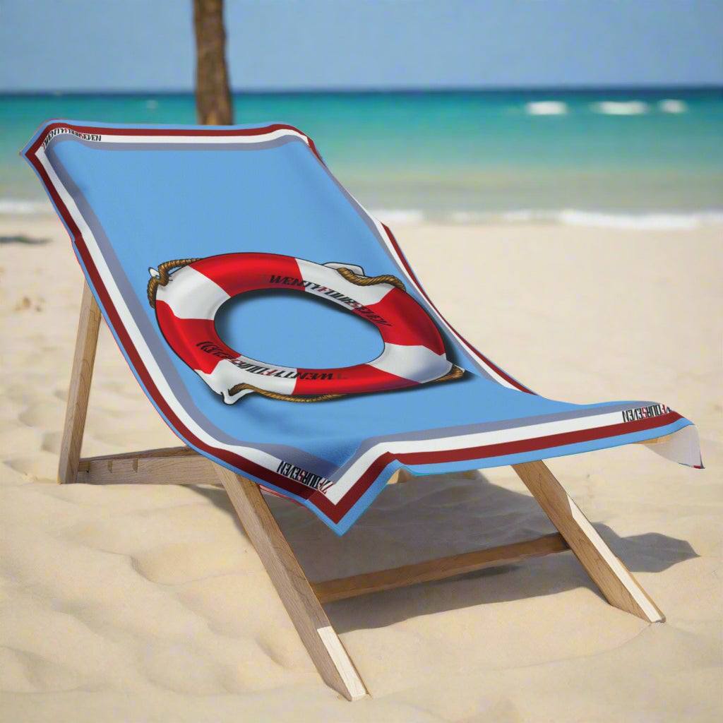 Oversized pool towel with a life belt graphic draped over a wooden beach lounger.