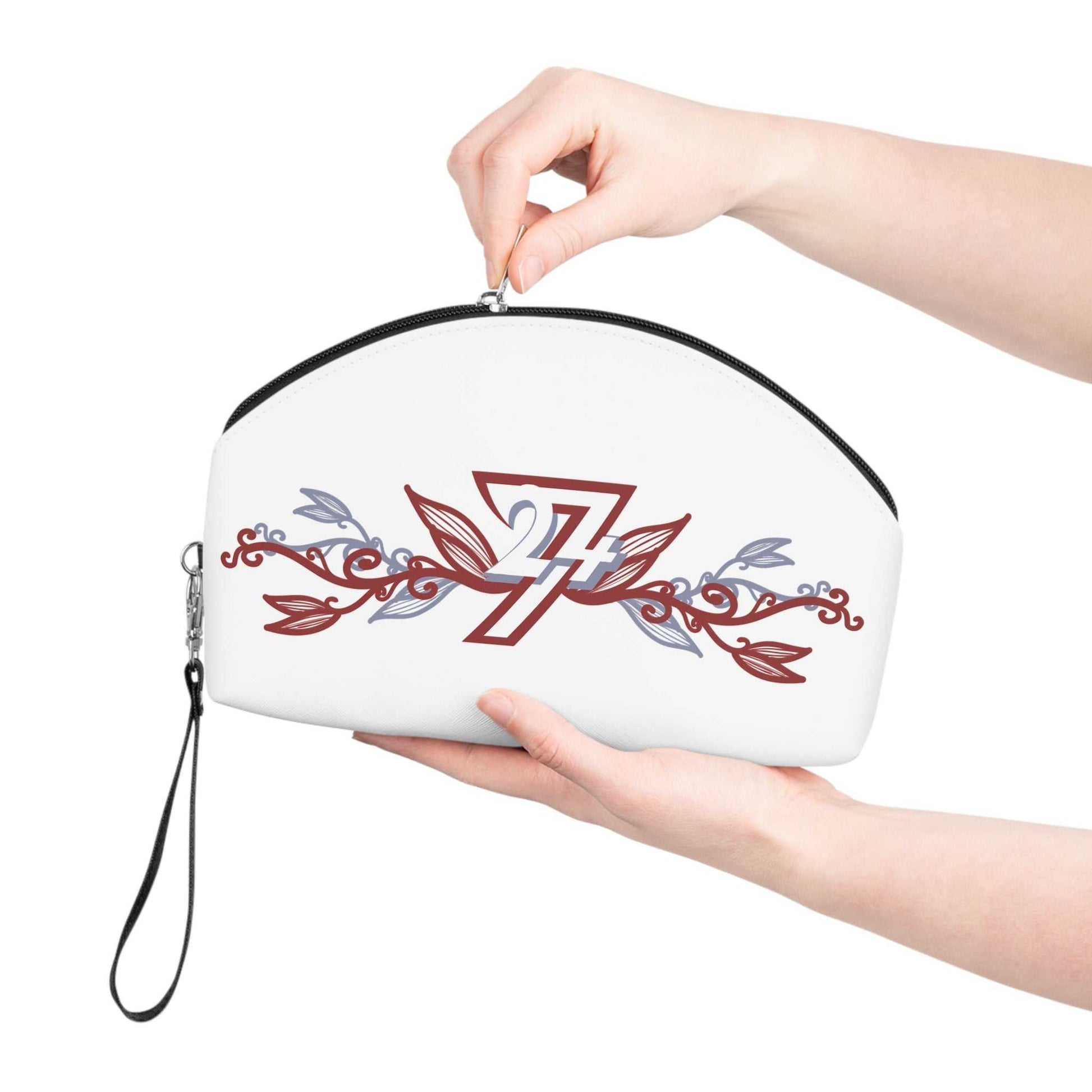A person's hands holding the white vegan leather cosmetic pouch, gently pulling the top zipper closed to demonstrate the bag's convenient size and the attached black wristlet strap.