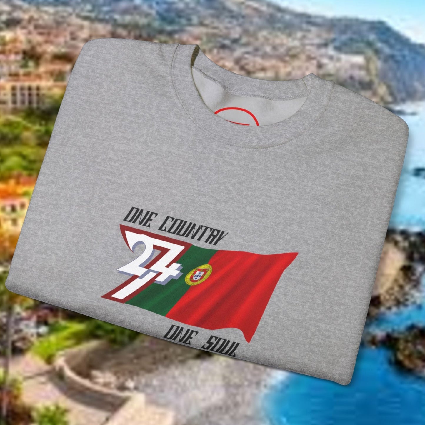 Gray Portugal flag sweatshirt with vibrant hand-drawn design folded on scenic coastal background