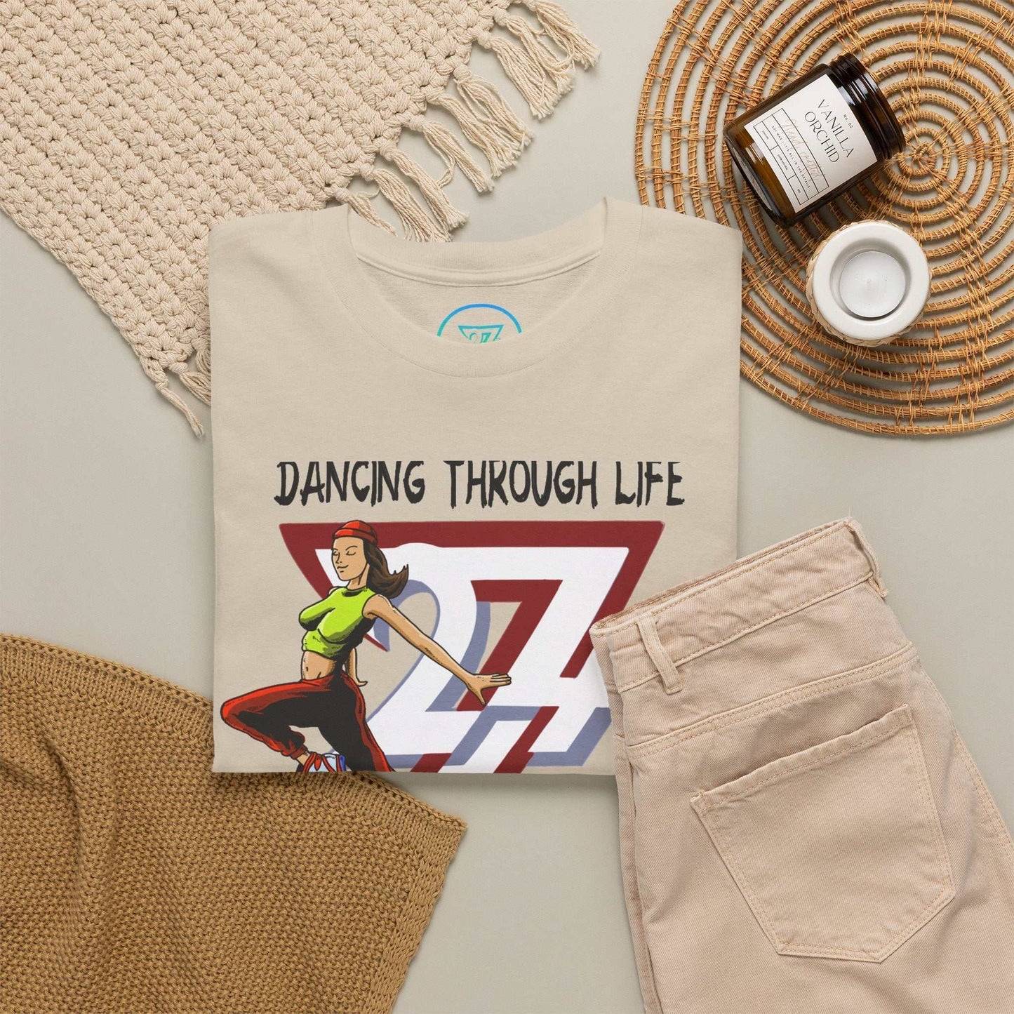 Aesthetic flat lay of a folded sand Dancing Through Life tee surrounded by similar light-colored urban streetwear garments, highlighting its relaxed city style.