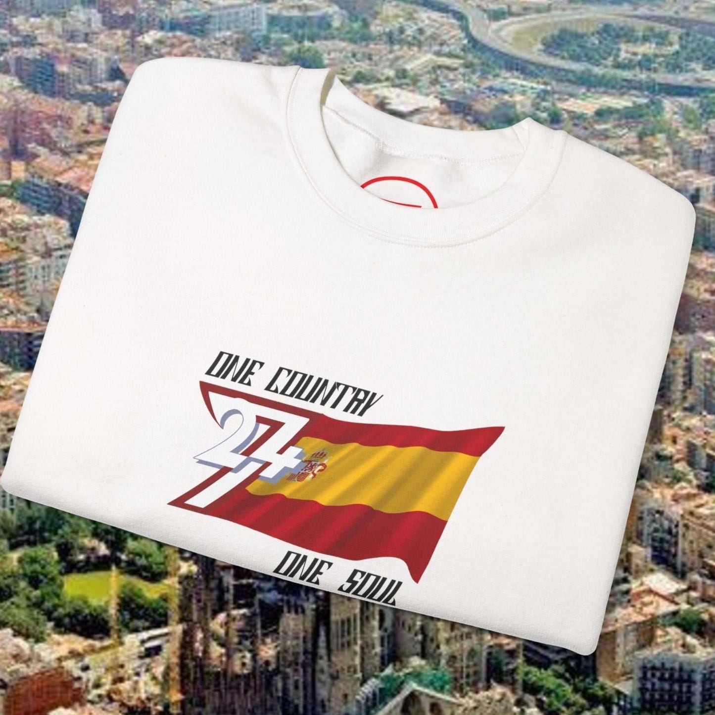 White Spain Flag Sweatshirt with hand-drawn flag graphic and "One Country One Soul" text folded on cityscape background