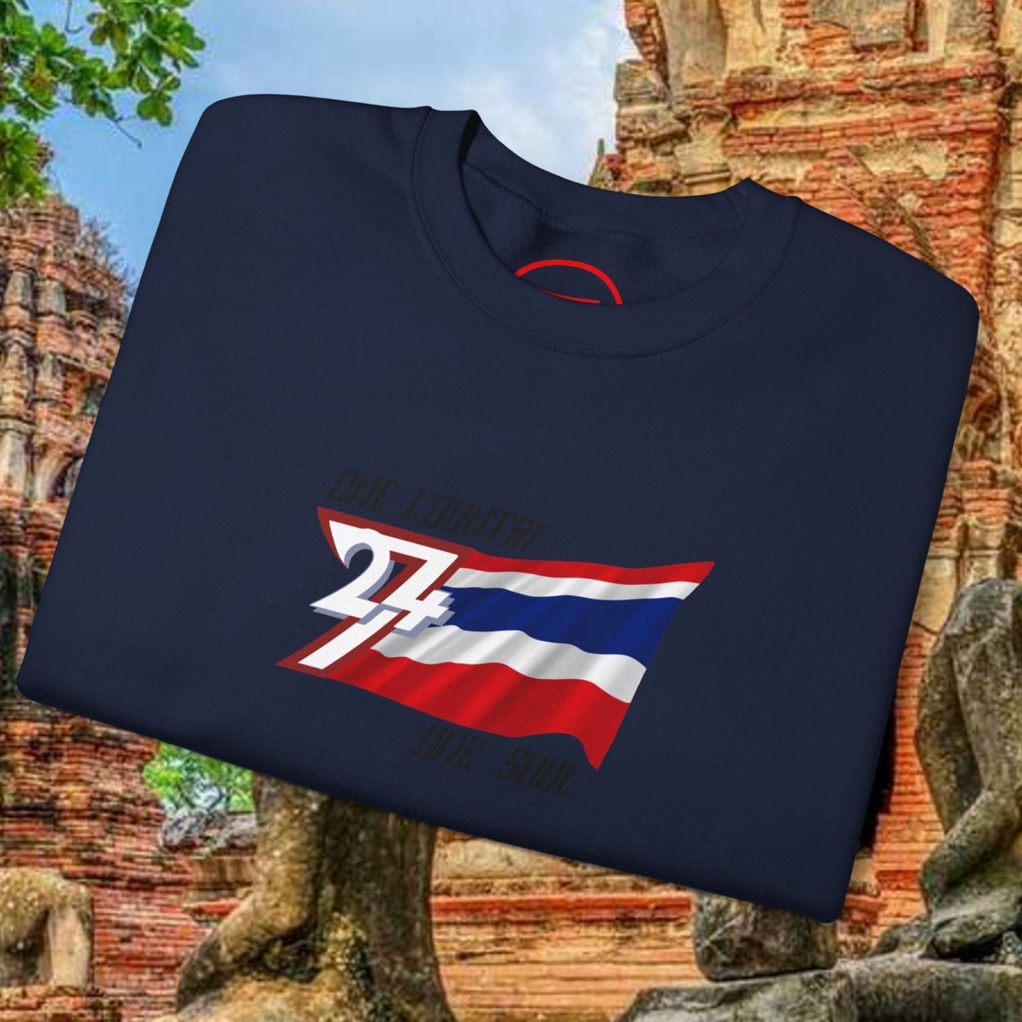 Folded navy blue crewneck sweatshirt featuring a hand-drawn Thailand flag graphic with "24" emblem, displayed outdoors near ancient Thai ruins.