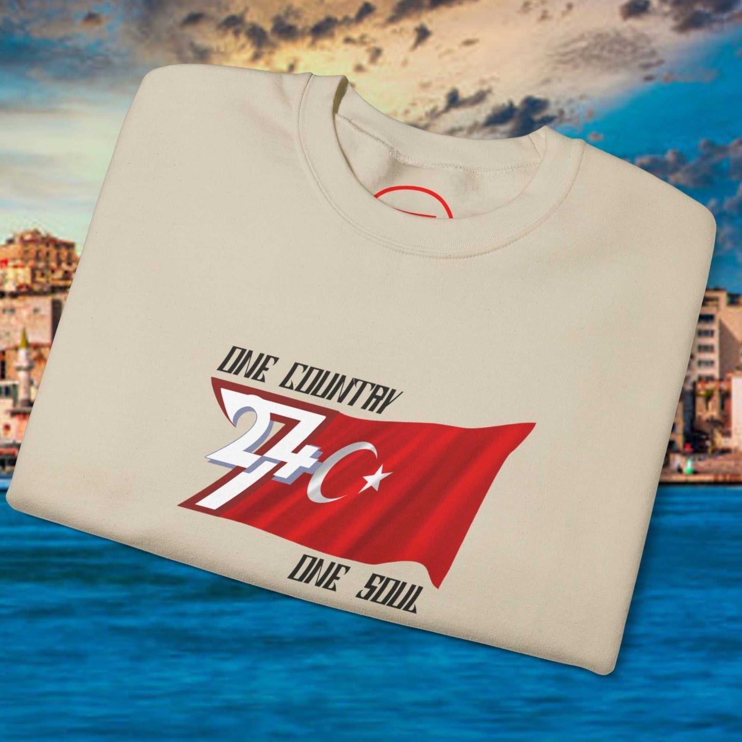 Folded beige Turkish flag sweatshirt with hand-drawn flag art and text "One Country One Soul" on vibrant waterfront background
