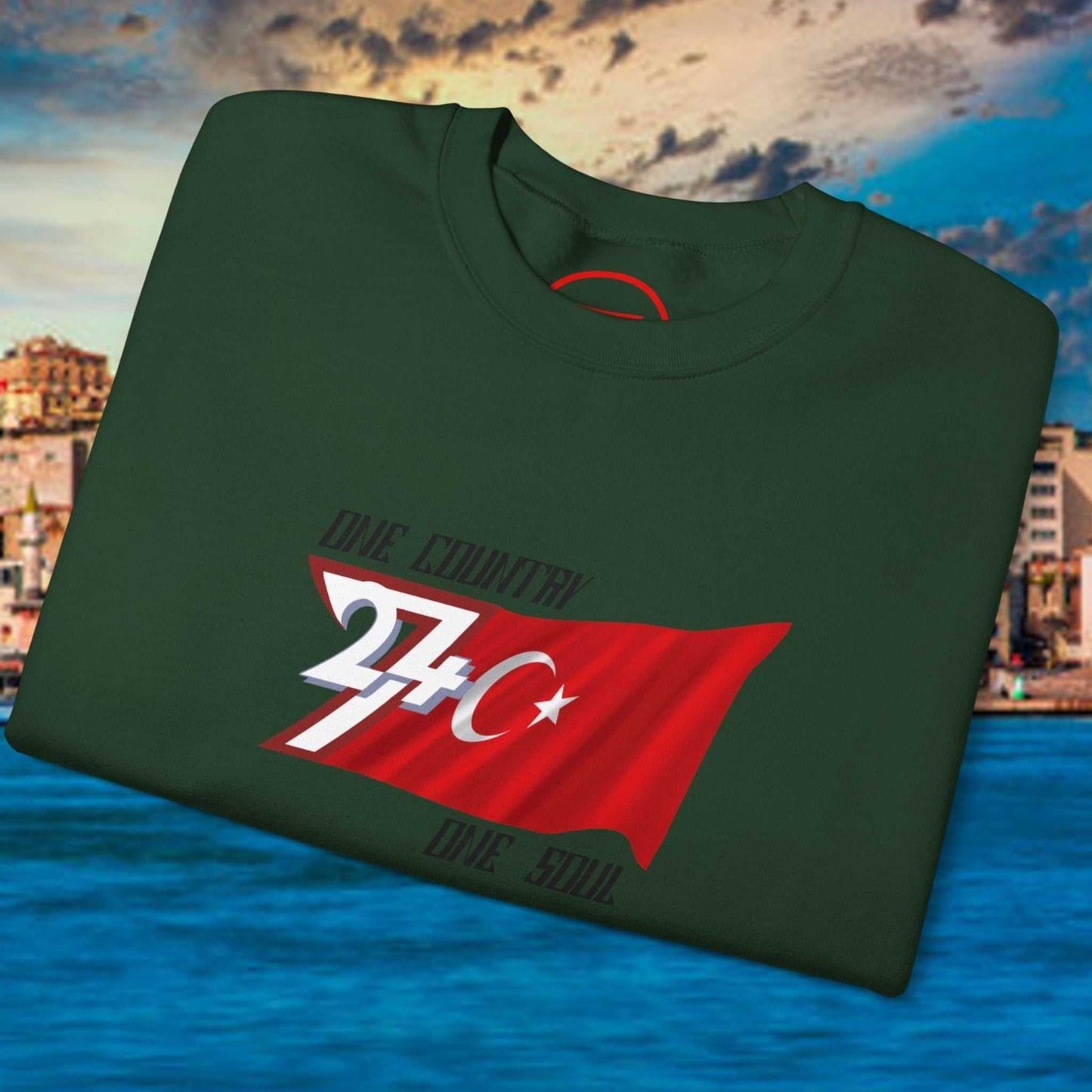 Folded dark green Turkish flag sweatshirt with hand-drawn red flag design and white crescent star on waterfront background