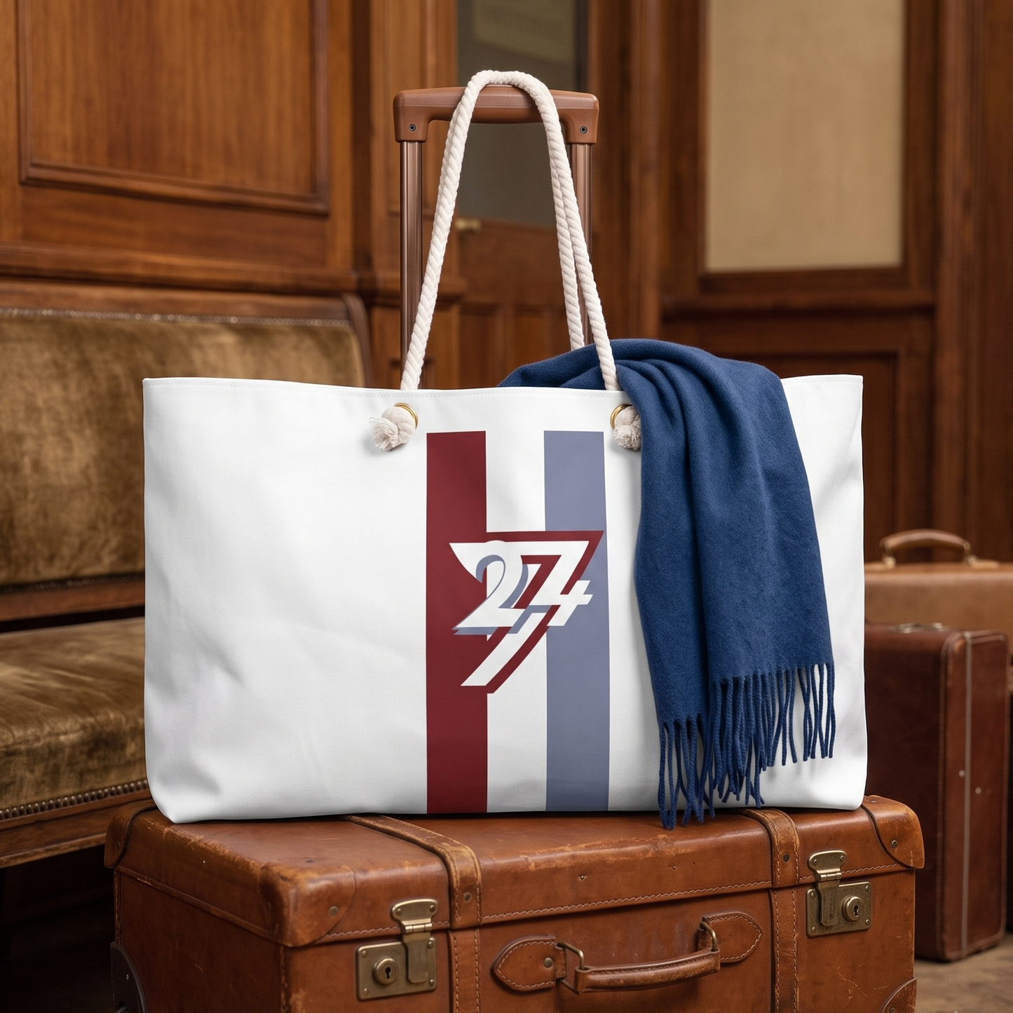 The 24/7 signature travel bag resting elegantly on top of vintage leather suitcases in a classic train station waiting room, highlighting the sporty racing stripes and sturdy cotton rope handles.