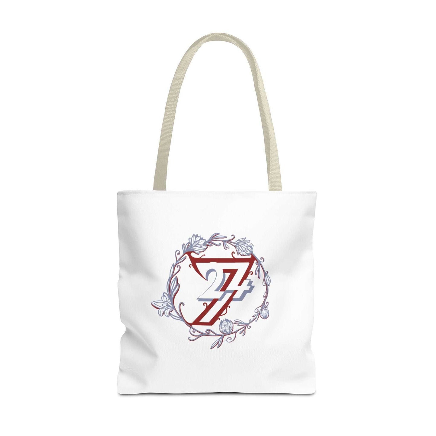A white canvas tote bag with two shoulder straps, featuring a central graphic of a red stylized letter 24/7 logo inside a white shield, surrounded by a circular floral wreath in muted blue-gray tones.