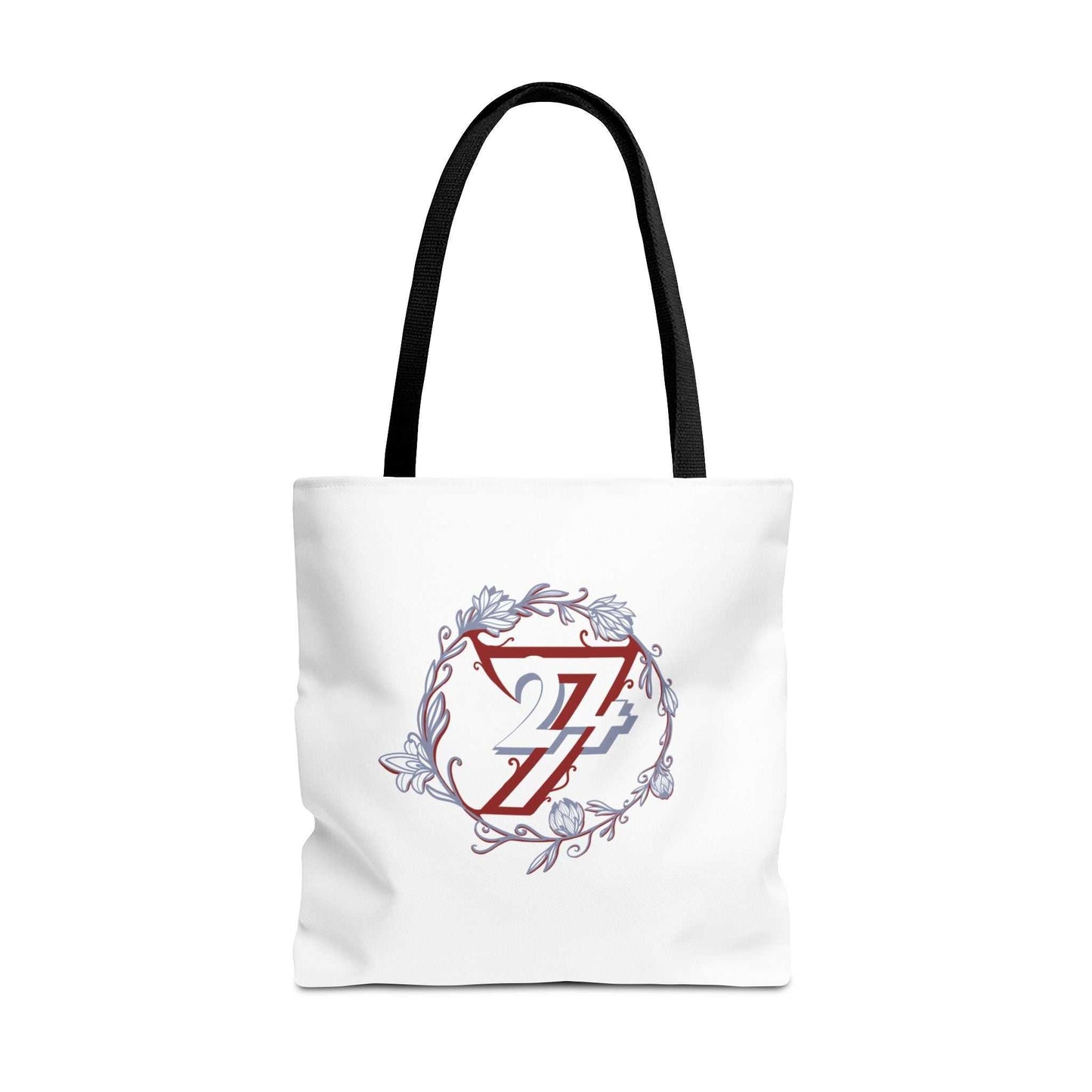 A white canvas tote bag with black shoulder straps, featuring a central graphic of a red stylized 24/7 logo enclosed in a circular floral wreath with light blue accents.