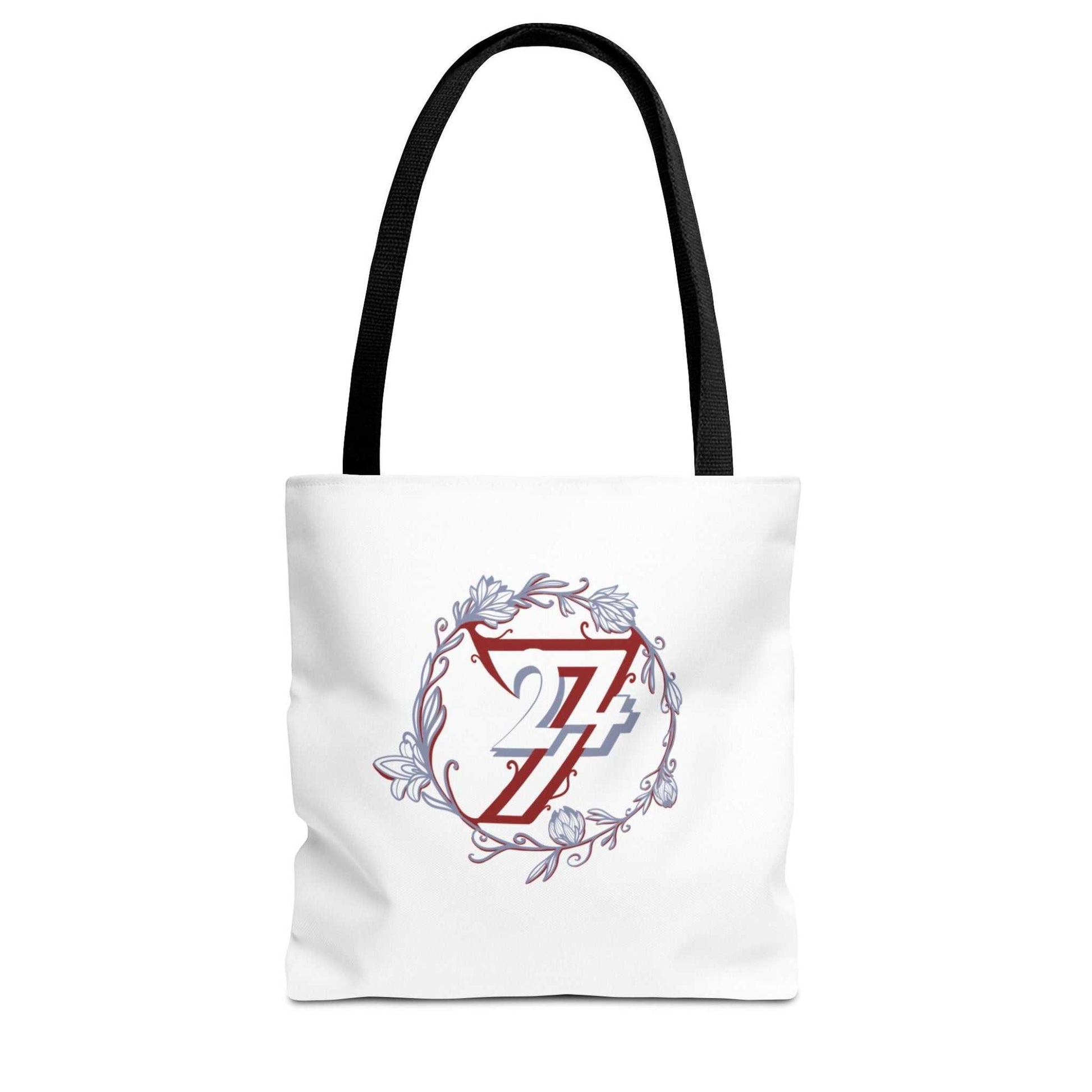 A white canvas floral tote bag with black shoulder straps, featuring a central graphic of a red stylized 24/7 inside a circular floral wreath with blue and gray accents.