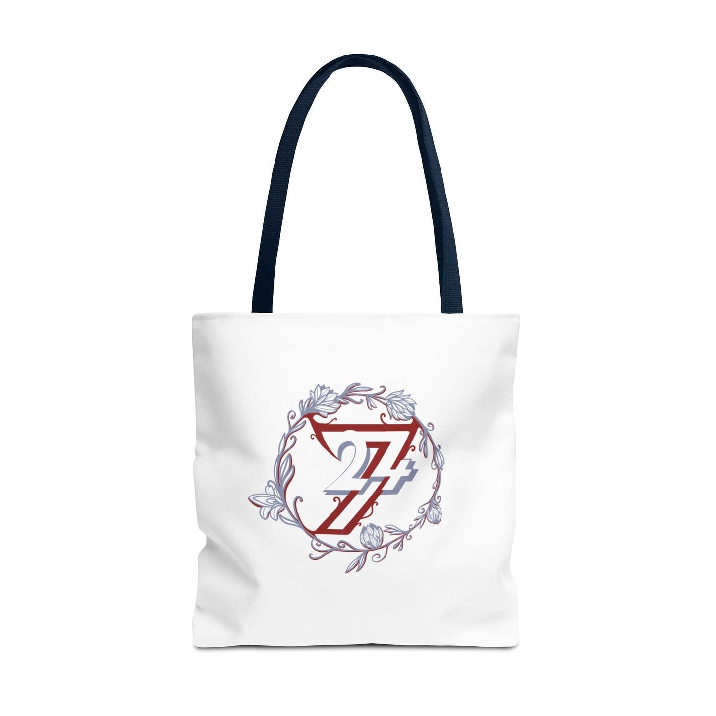 A white canvas tote bag with dark navy blue shoulder straps, featuring a central graphic of a red and blue 24/7 logo enclosed in a circular floral wreath with light blue accents.